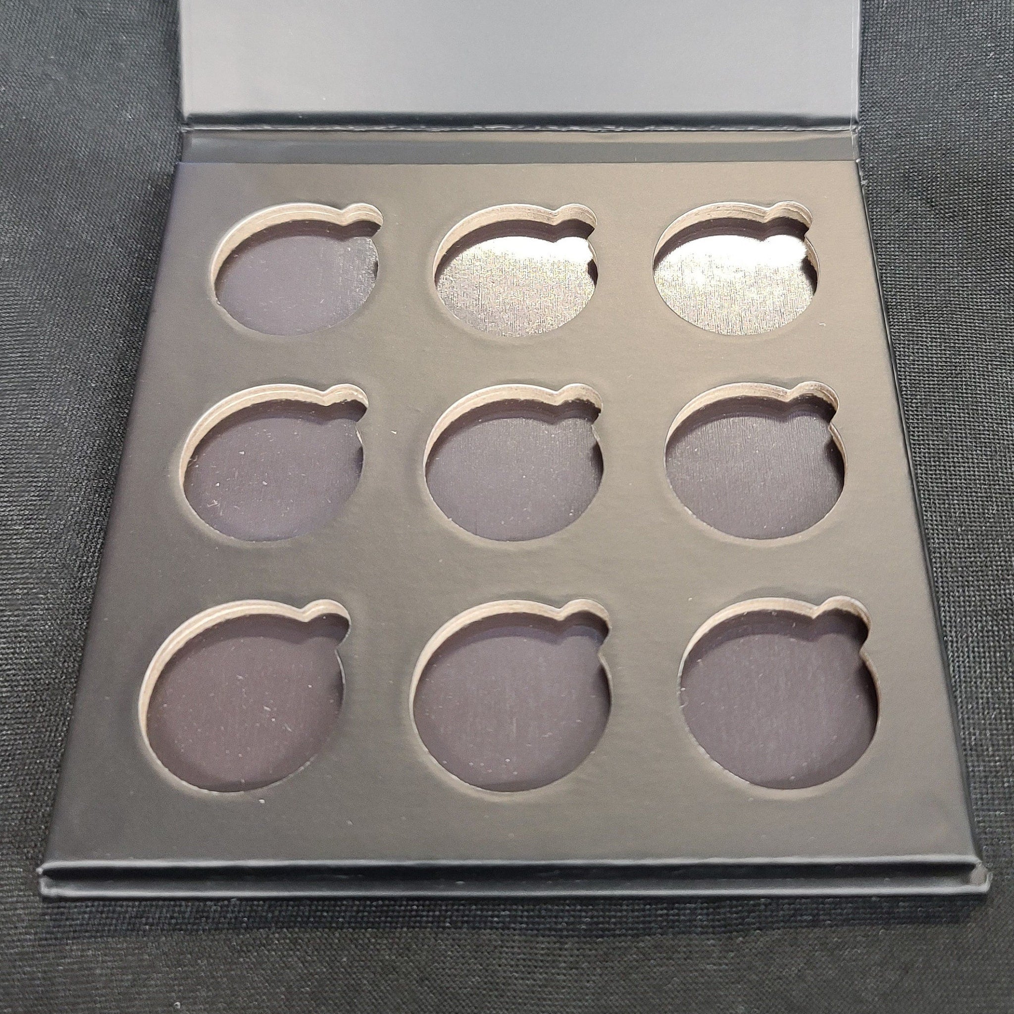 Close-up of matte black eyeshadow palette showing nine smooth, pigmented square pans in magnetic case