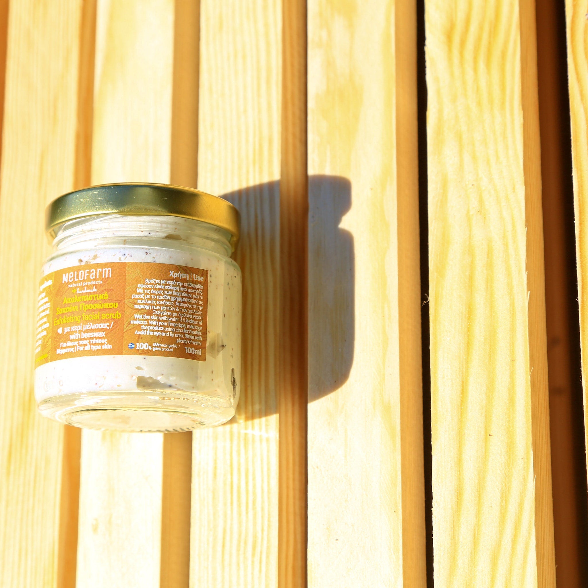 Exfoliating facial scrub in glass jar with gold lid, on wooden background, Melofarm brand