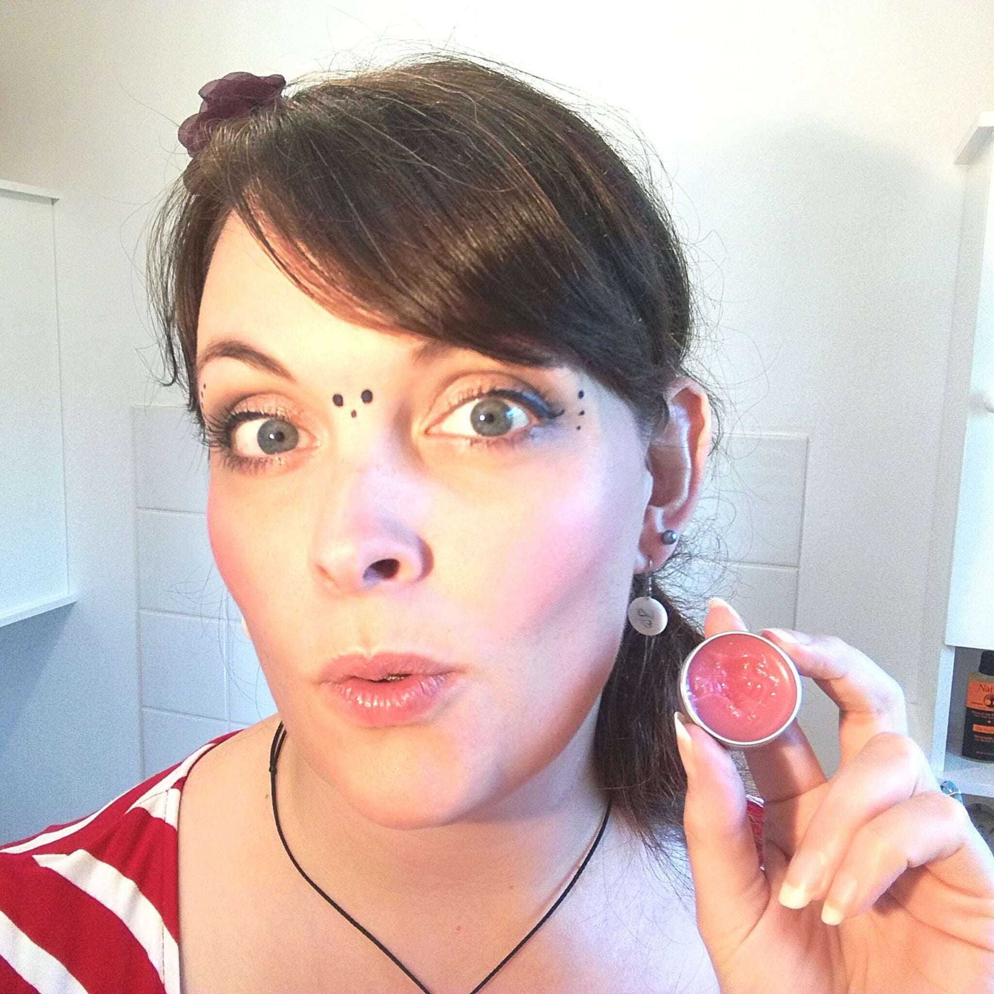 Lip balm in round silver container, pink color, held by person