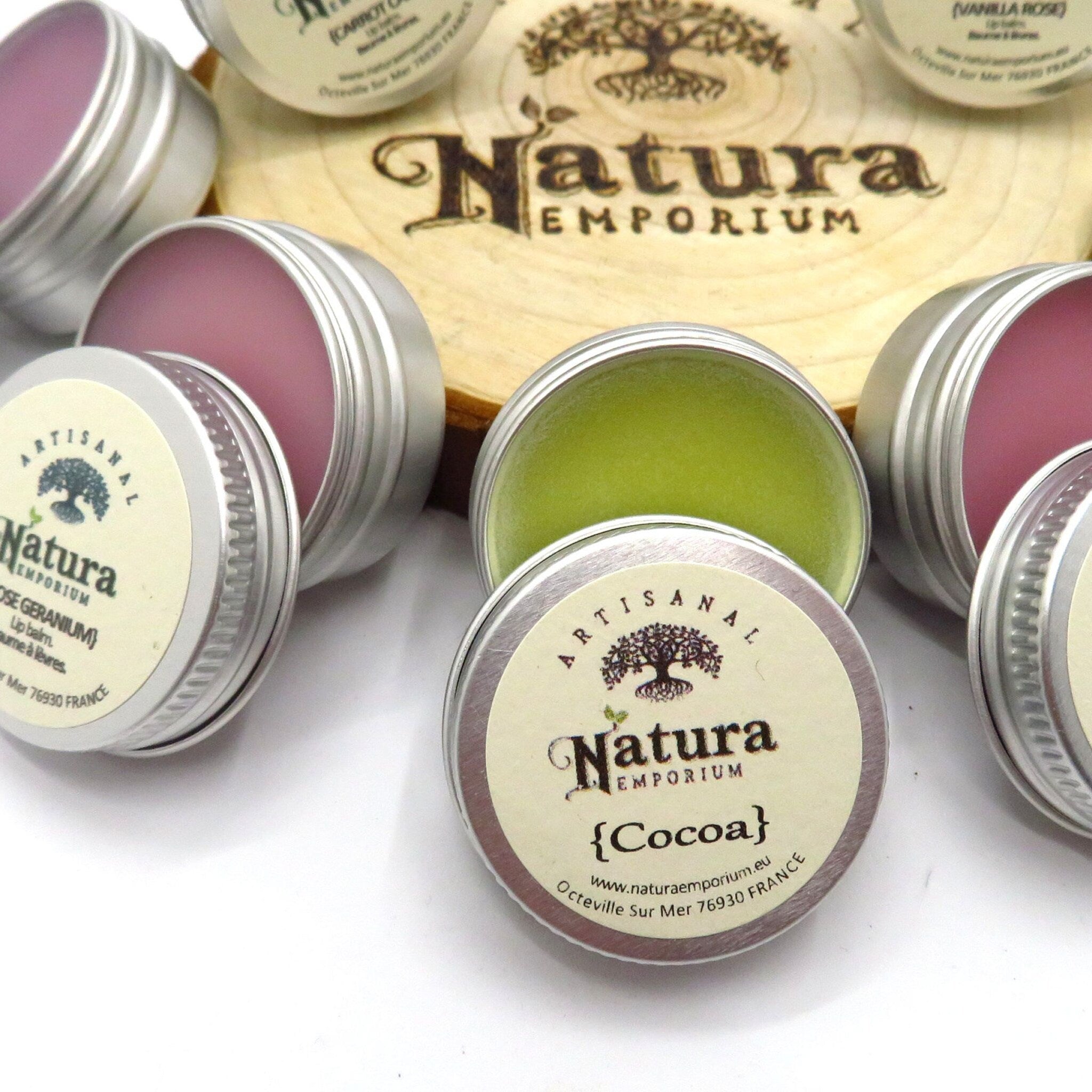 Lip balm tins with silver metal lids, Natura Emporium logo, and colored balm inside