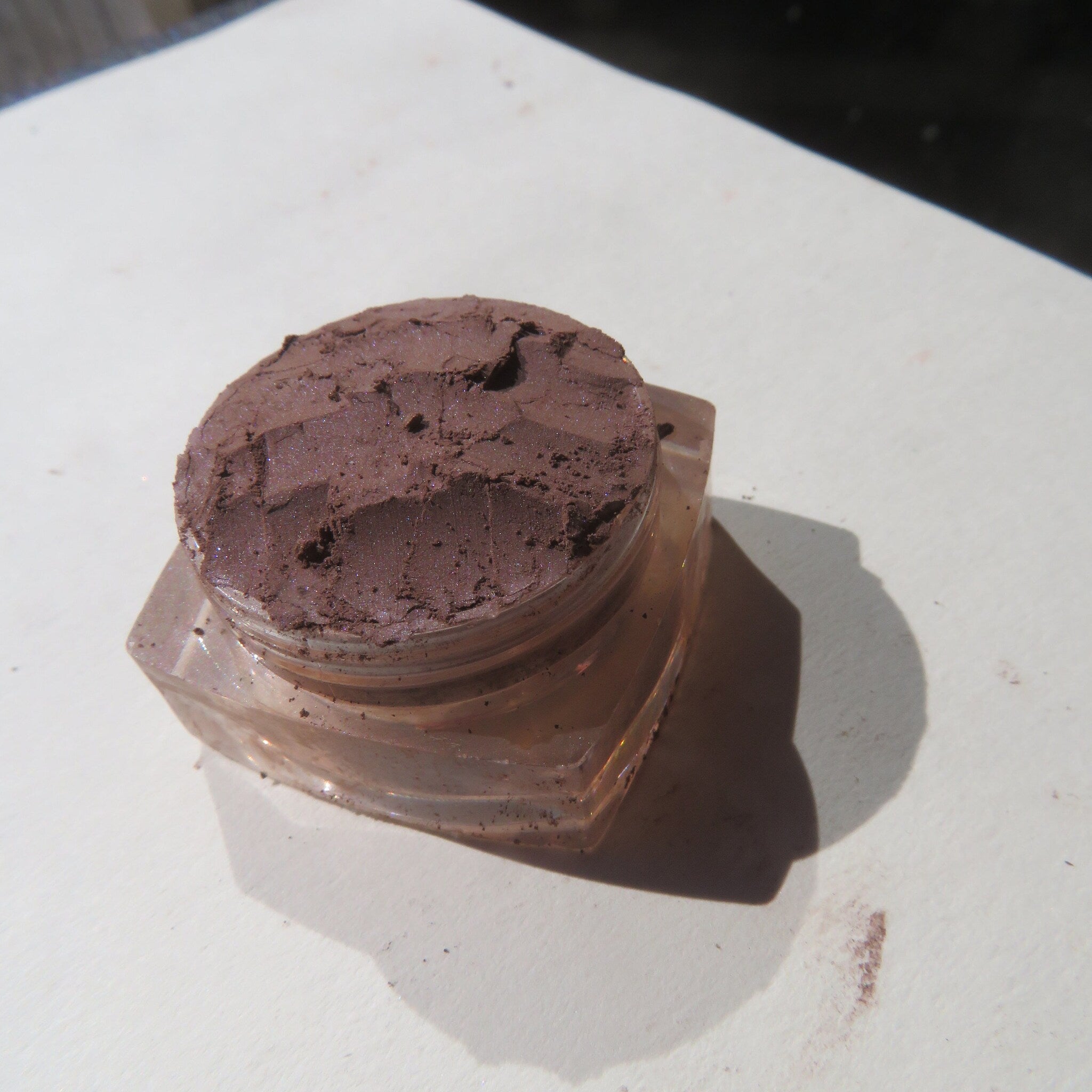 Eyeshadow, dark brown powder, clear glass jar, cosmetic product