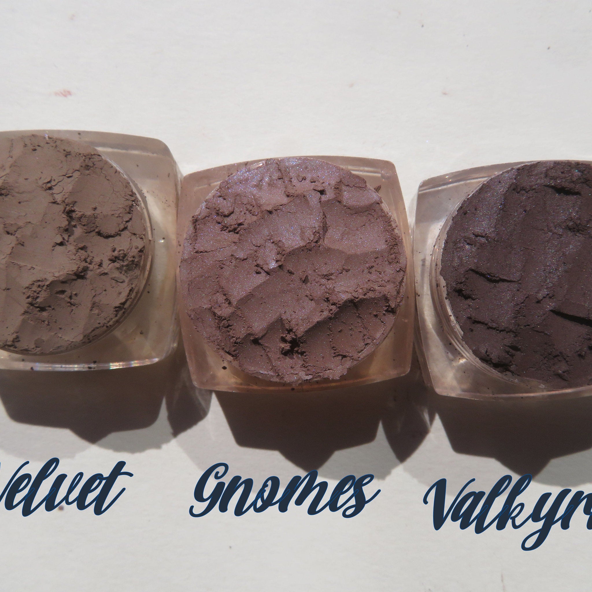 Eyeshadow pots with brown, tan, and dark purple powder in clear containers, "Velvet" "Gnomes" "Valkyrie" text