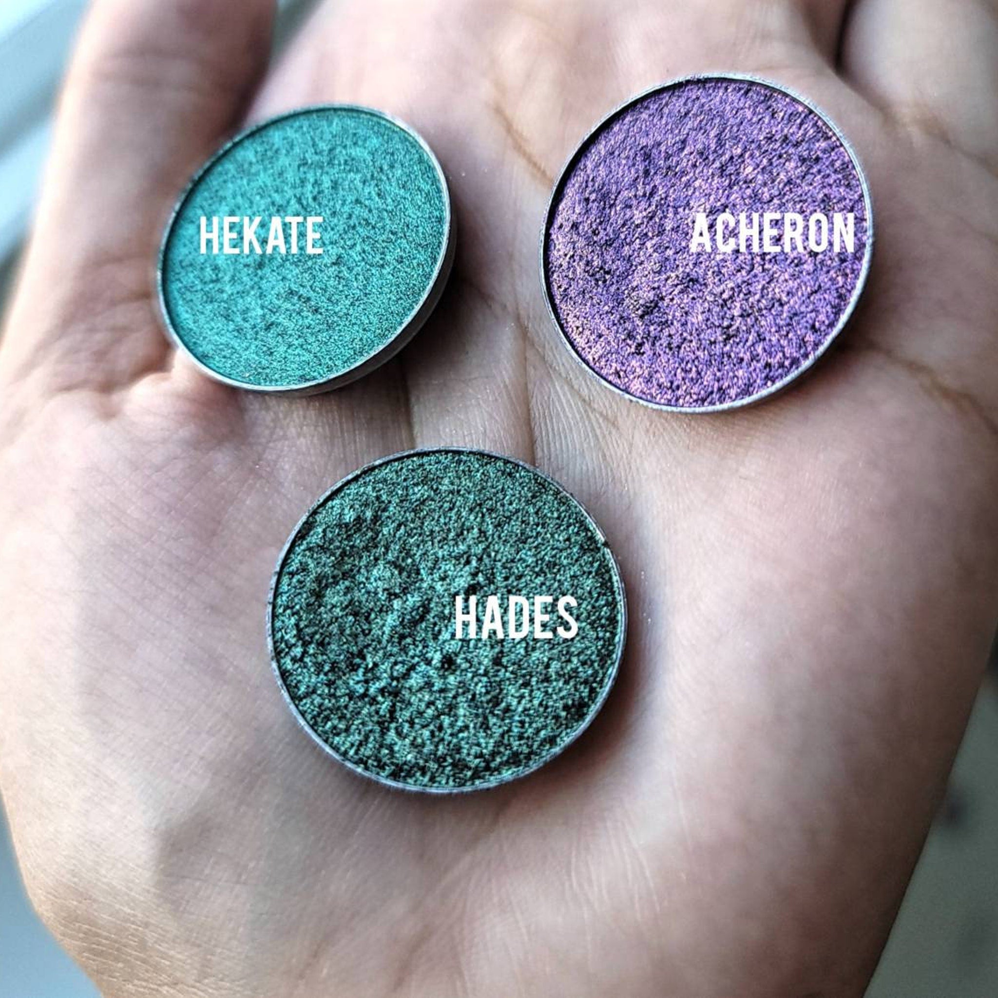 Gold and emerald green multichrome eyeshadow pot with reflective lid, displayed on sleek black packaging