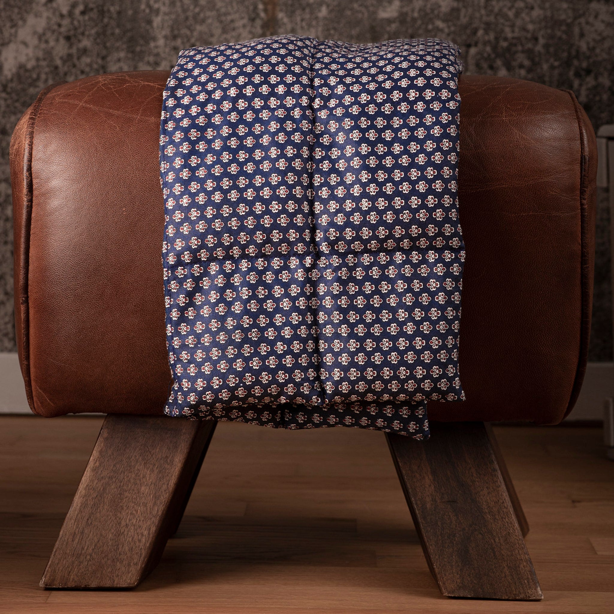 Patterned fabric, navy blue with floral print, draped over brown leather stool