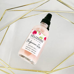 Facial cleanser bottle, pink liquid, black pump, Delizioso Skincare label, rose design on a mirrored surface