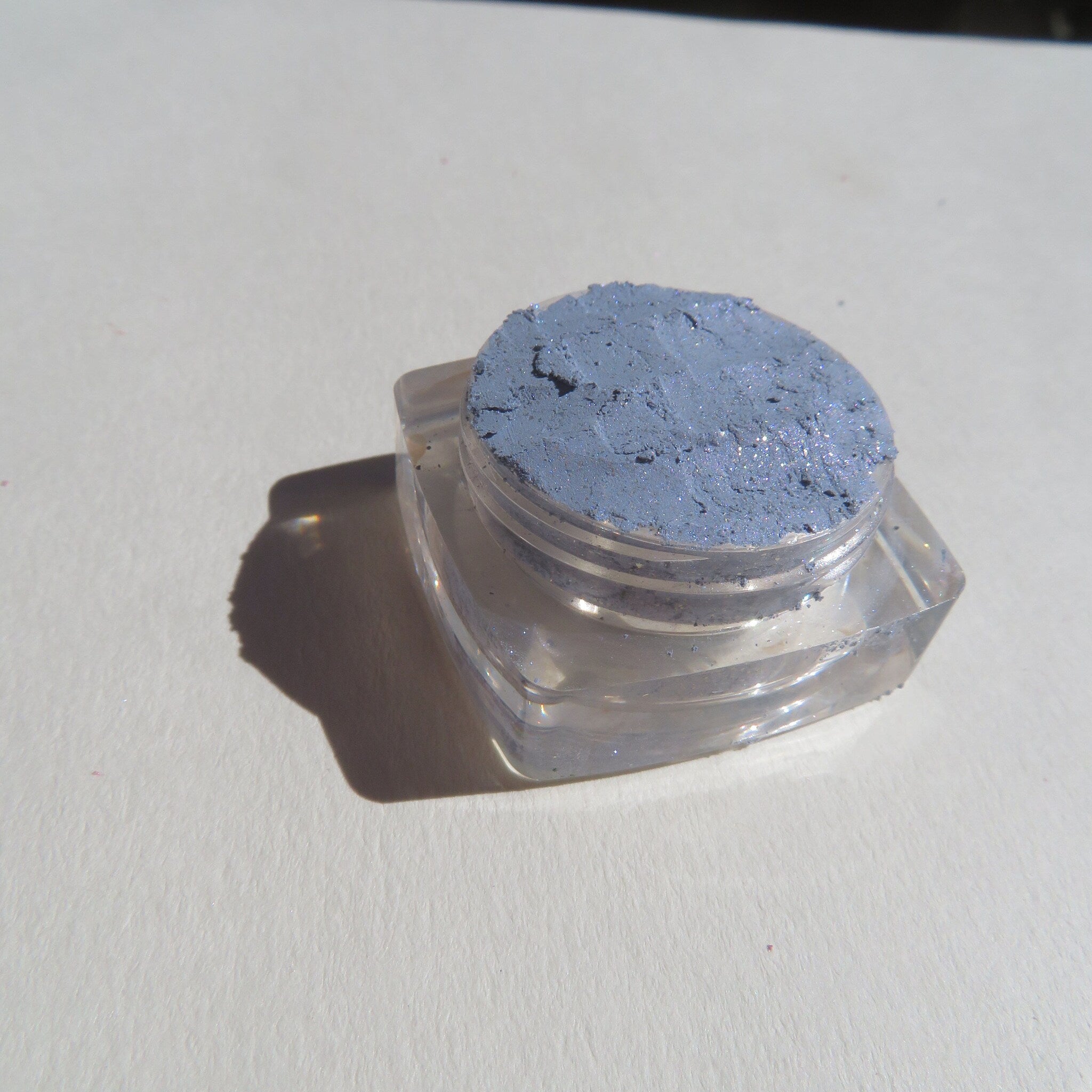 Hand applying sparkly blue-gray mineral eyeshadow with fingertip, showing shimmer pigment dispersion