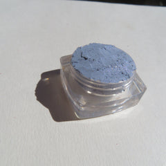 Hand applying sparkly blue-gray mineral eyeshadow with fingertip, showing shimmer pigment dispersion
