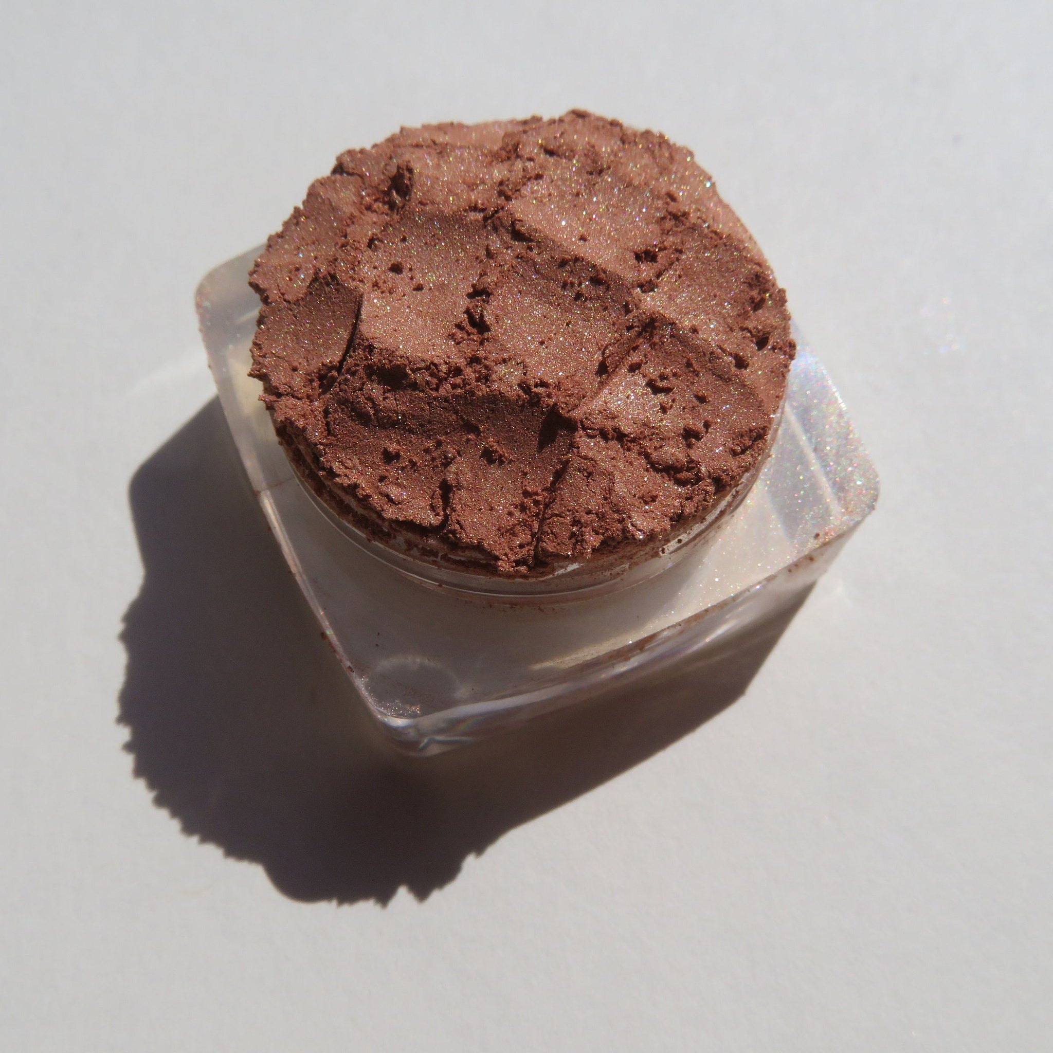 Side view of loose mineral eyeshadow in bronze copper brown shimmer, showcasing fine powder texture and reflective particles