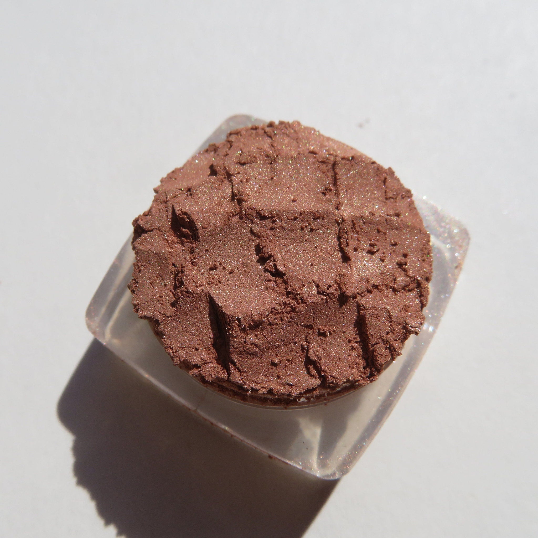 Bronze copper brown loose mineral eyeshadow in clear jar with black screw-top lid on marble surface