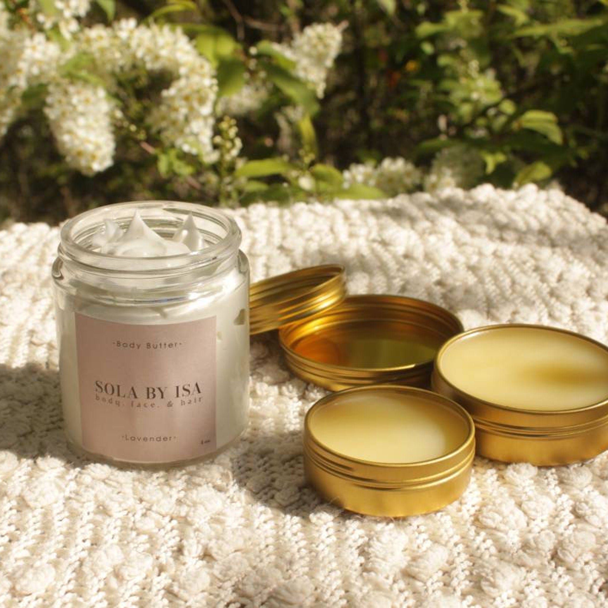Body butter jar with white cream, gold tins, and textured off-white fabric, Sola by Isa brand