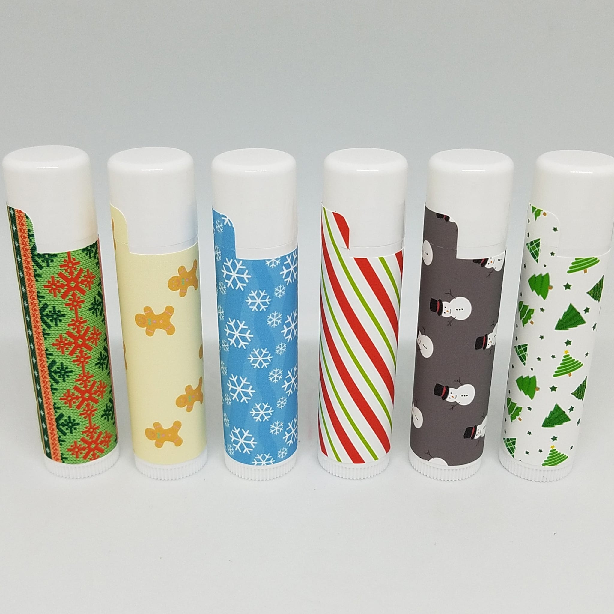 Lip balm tubes with various patterns, including snowflakes, snowmen, and Christmas trees
