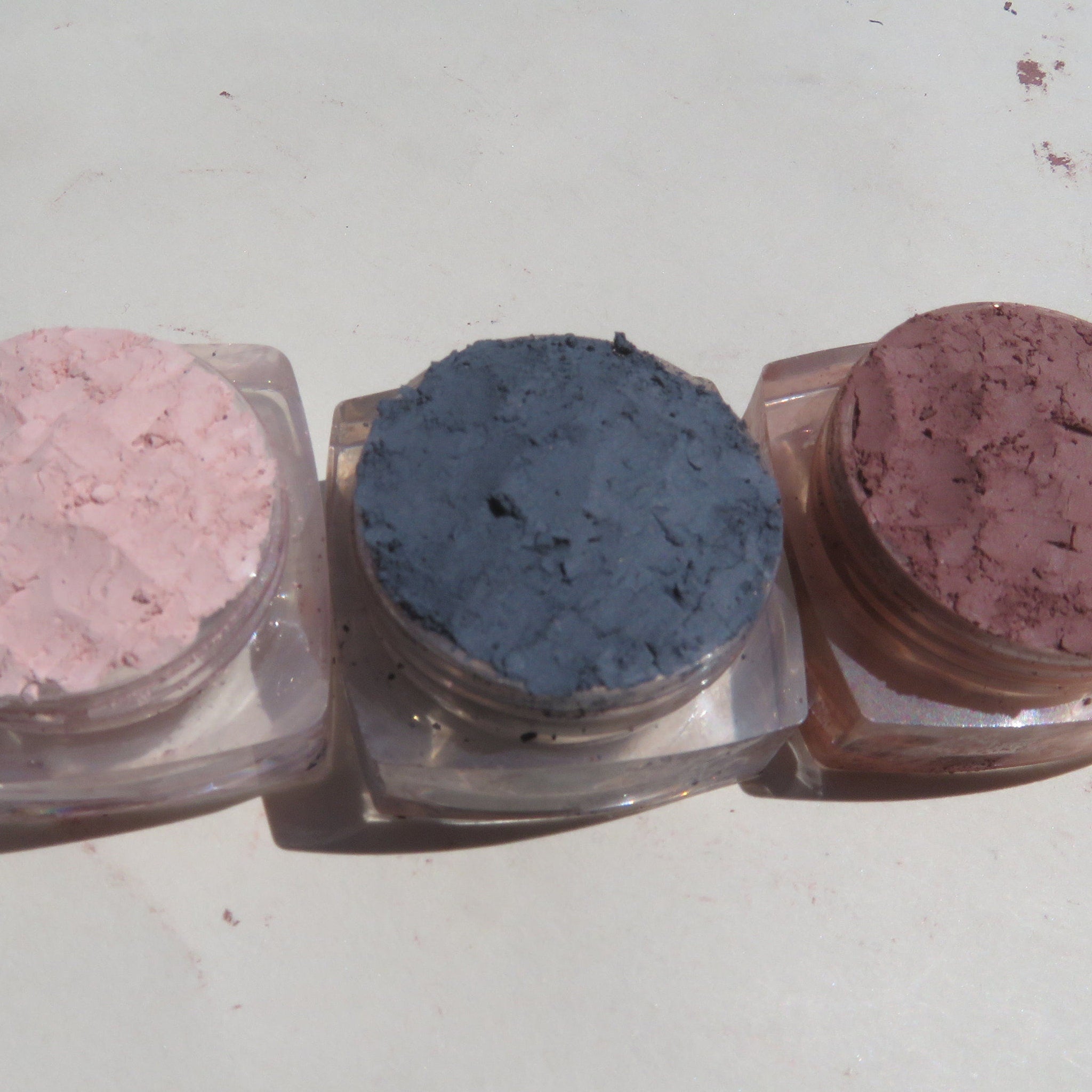 Side view of three matte loose mineral eyeshadows in glass jars showing vegan pigments in earthy tones with sifter lids