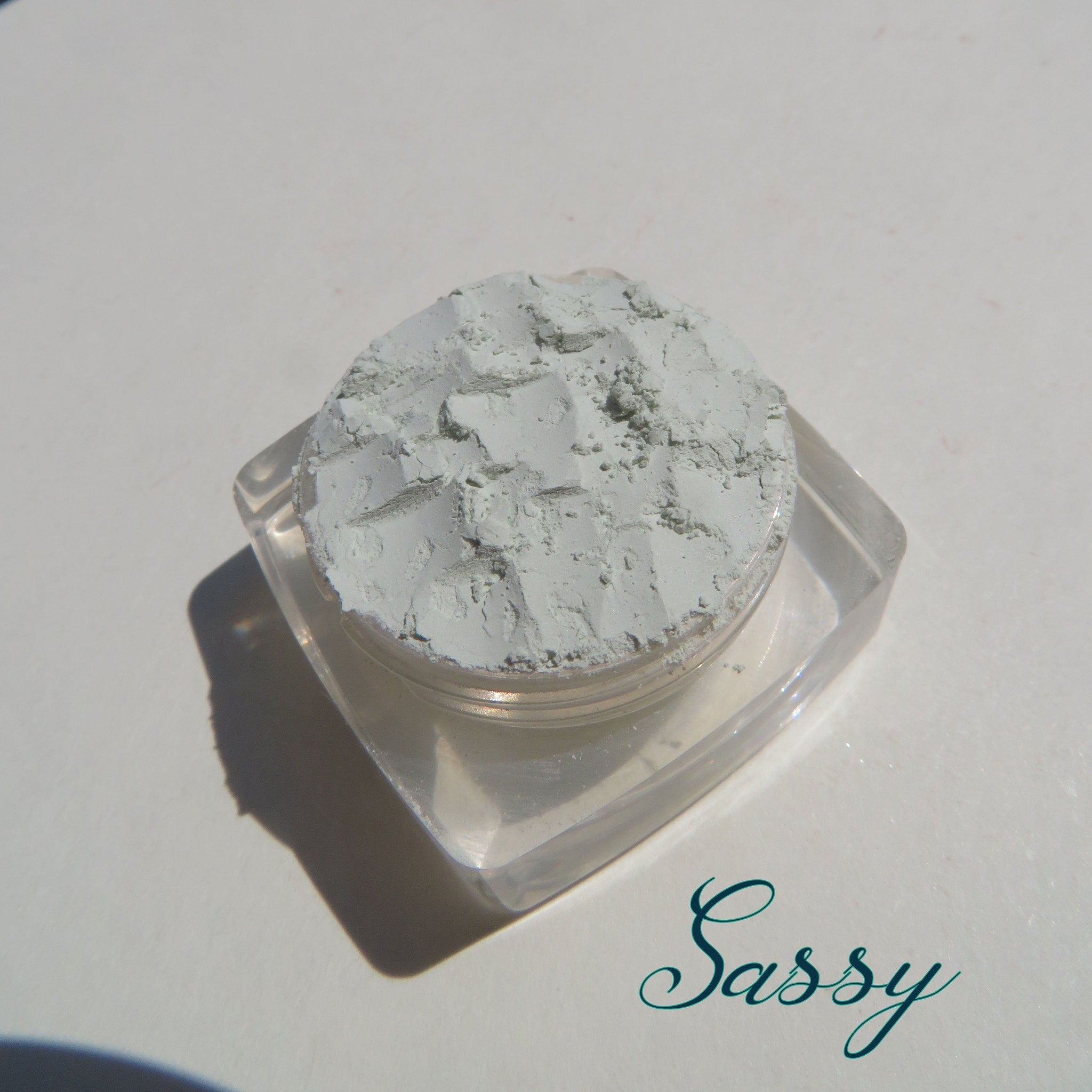 Close-up of matte pale green loose mineral eyeshadow with fine powder texture in eco-friendly packaging