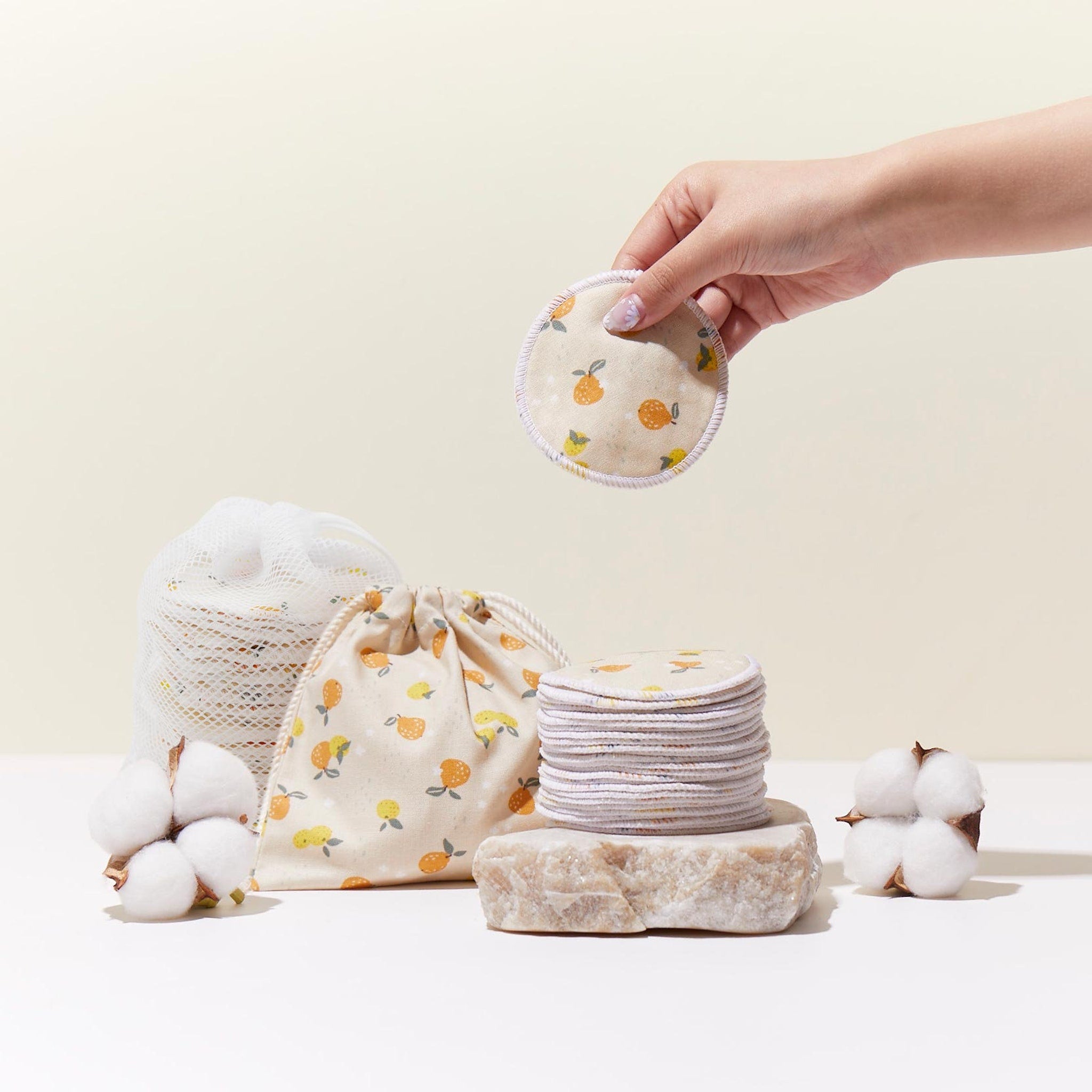 Reusable makeup remover pads with fruit pattern, round, beige with white trim, held by hand