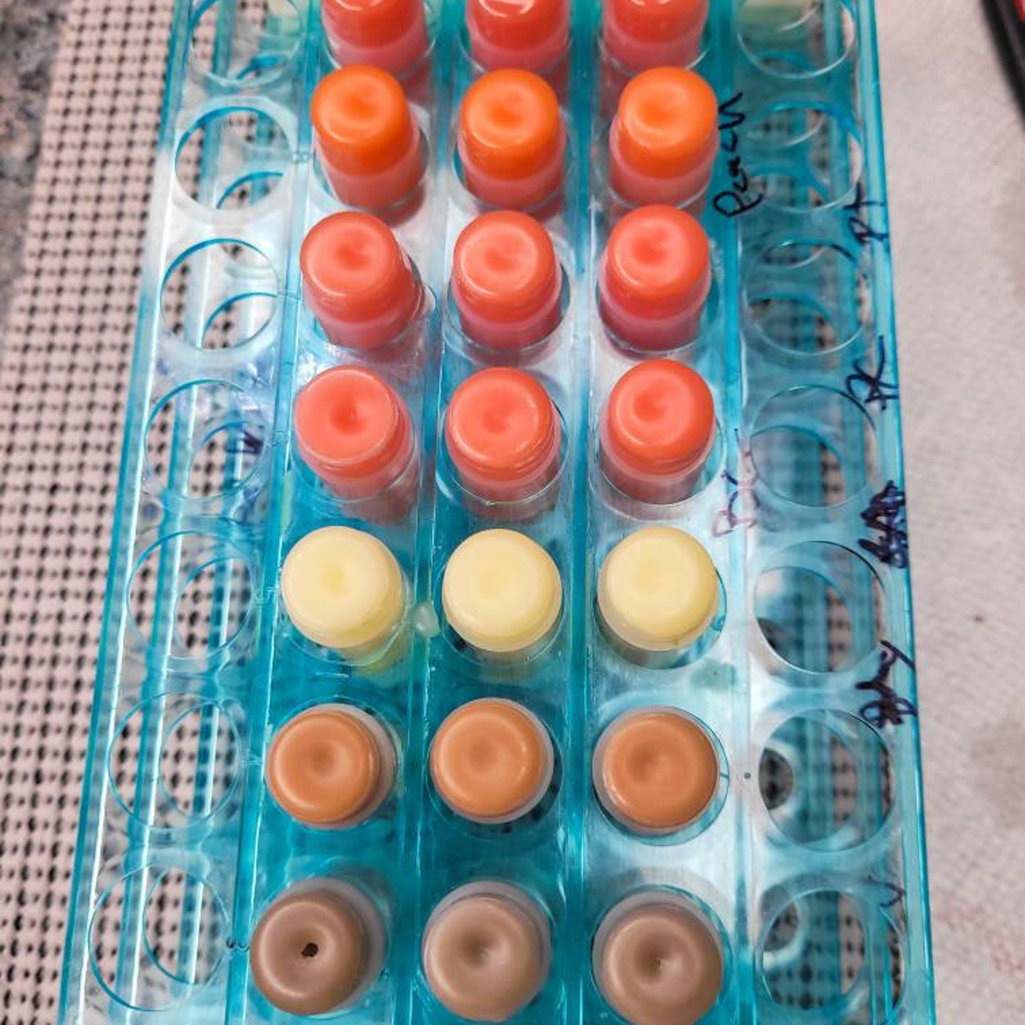 Lip gloss samples in various colors, arranged in a blue plastic tray, for testing