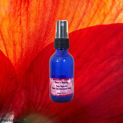 Blue glass spray bottle with black cap, red and orange background, Bear's Beauty label