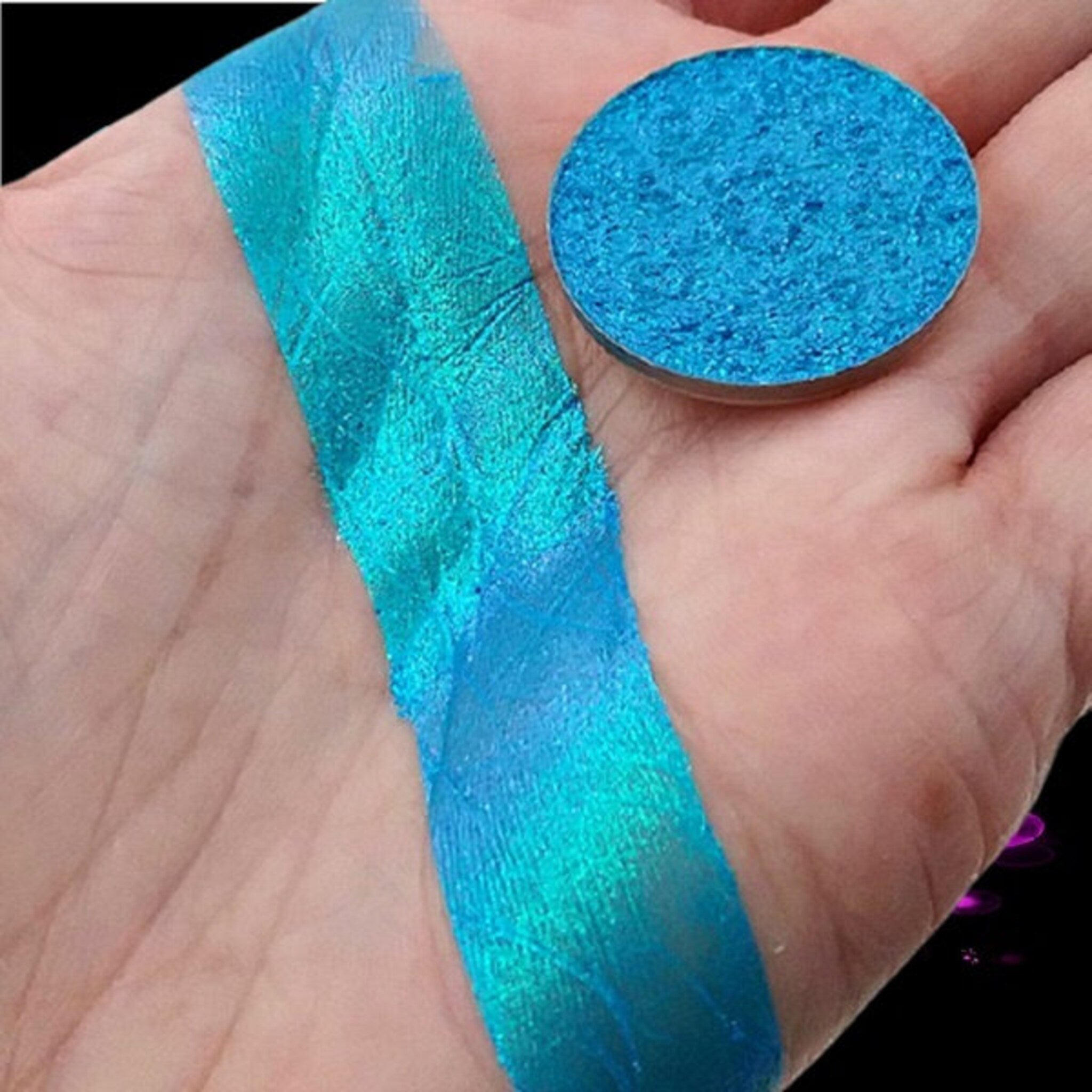 Close-up of duochrome Infinite Aster eye shadow pan showing shifting violet-blue shimmer in compact packaging