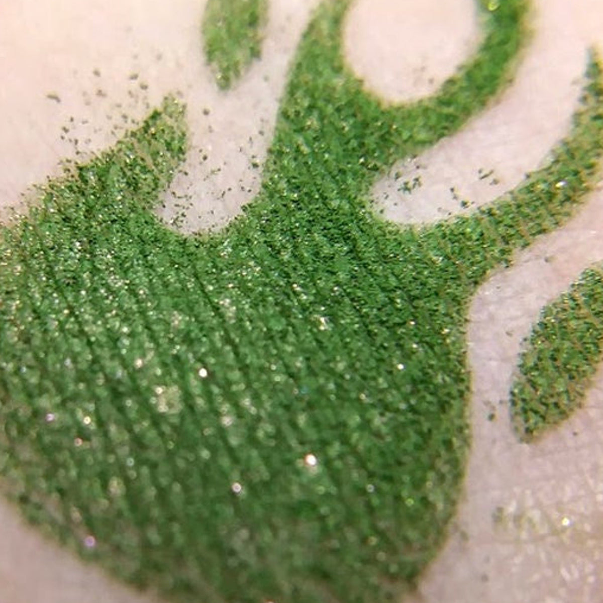 Close-up of vegan green eyeshadow pan with red duochrome shift and sparkling flecks, named Karaoke Demon