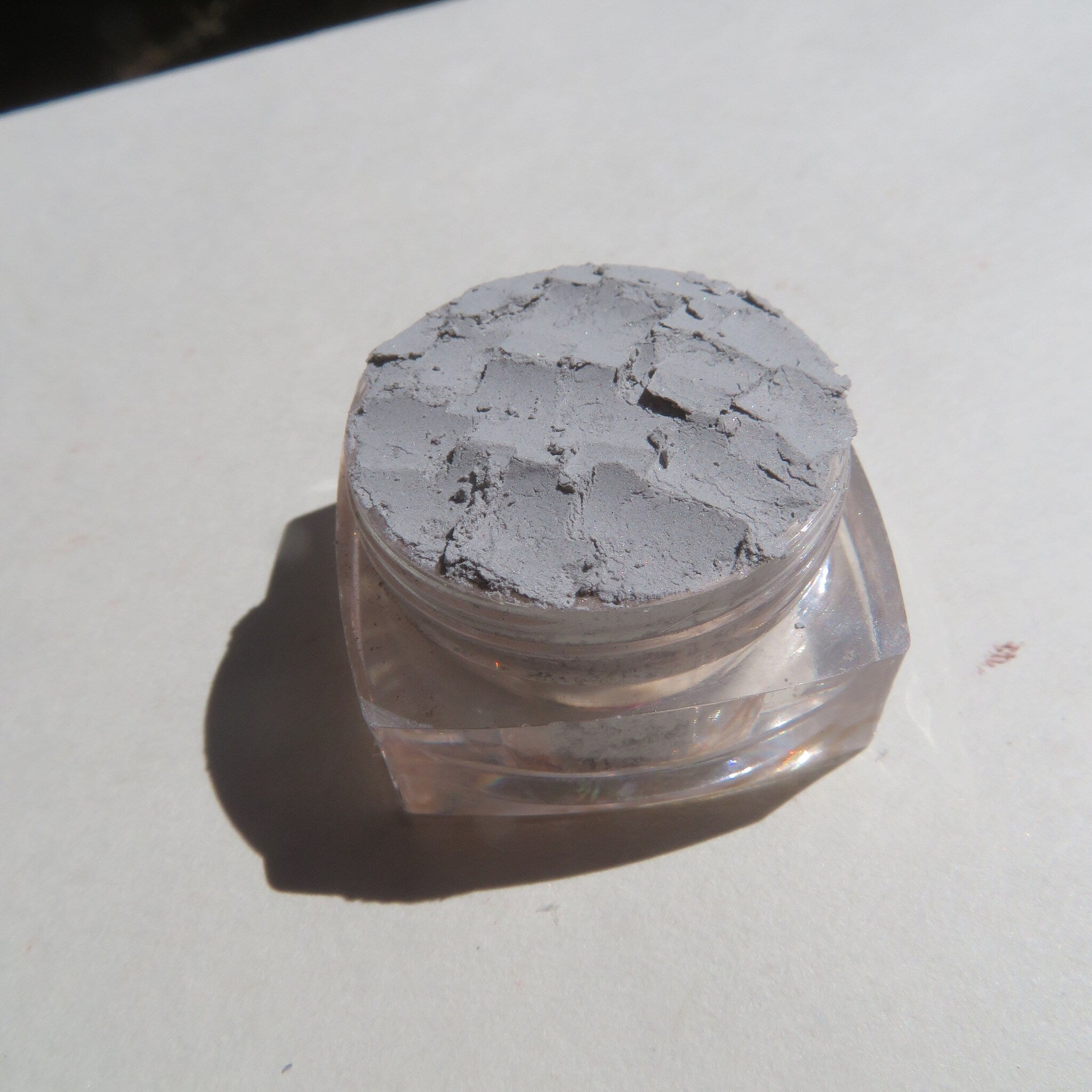 Hand applying pale matte gray mineral eyeshadow with a fluffy brush onto eyelid for soft smoky look