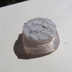 Hand applying pale matte gray mineral eyeshadow with a fluffy brush onto eyelid for soft smoky look