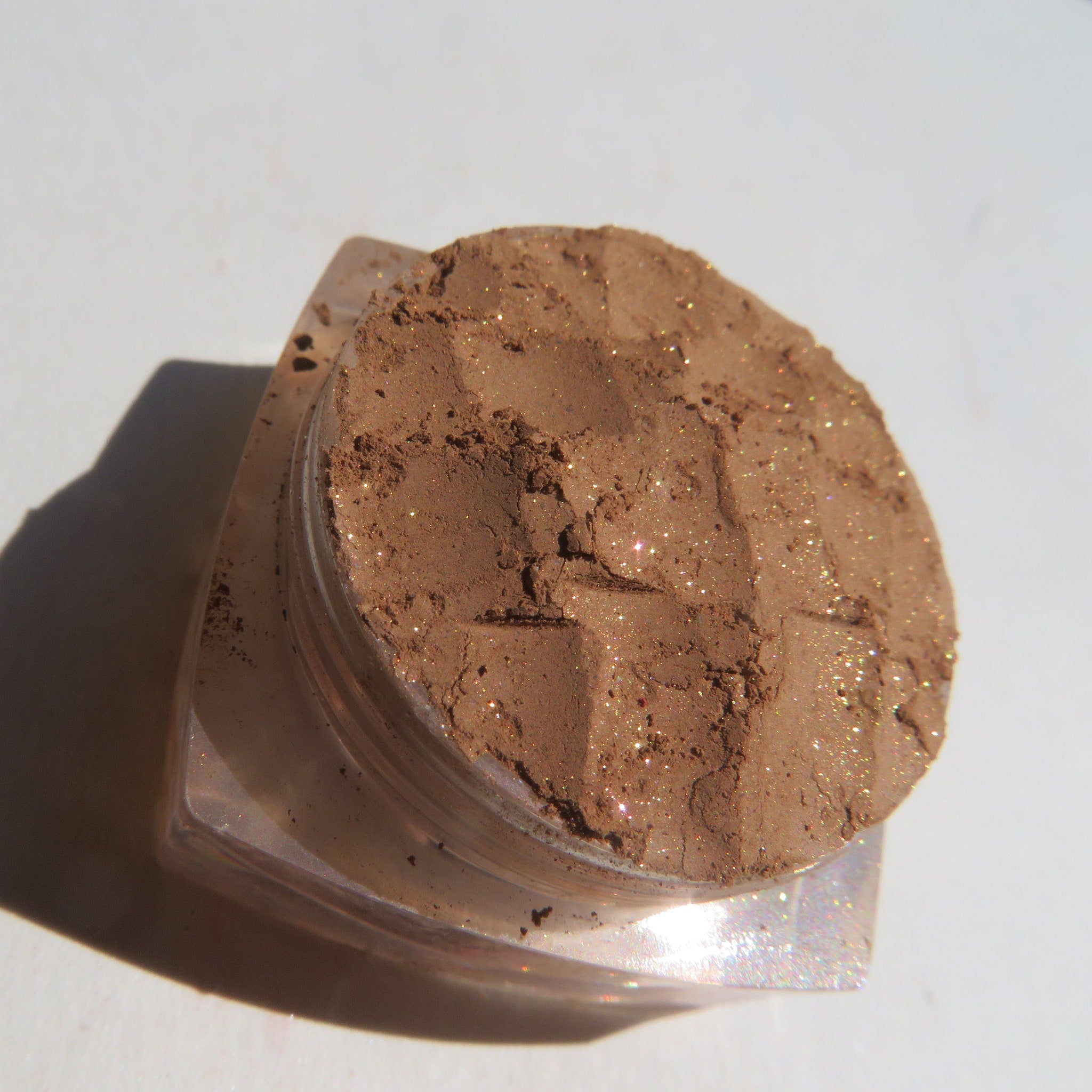 Side view of golden brown loose powder eyeshadow shimmering in light with vegan label visible
