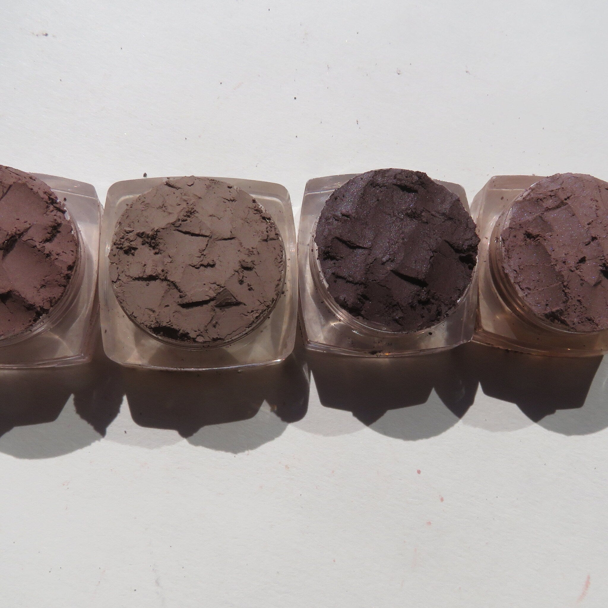 Side view of four matte brown vegan loose mineral eyeshadows in round containers with sifter lids, showcasing texture.