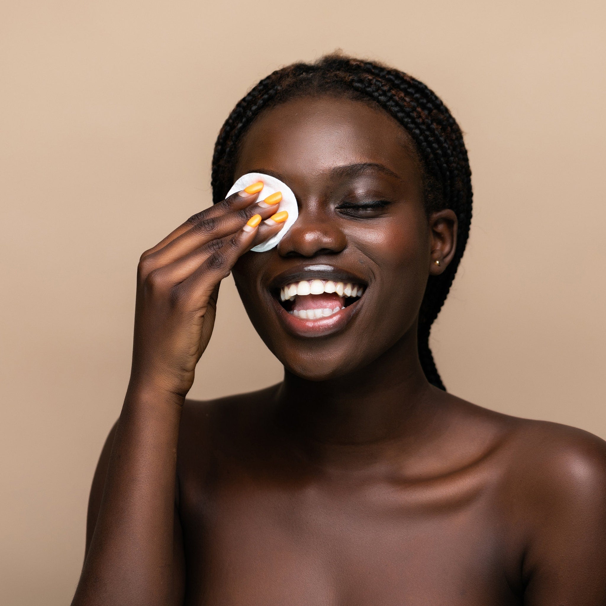 Cotton pad white, woman using to wipe face, with orange nail polish and dark skin