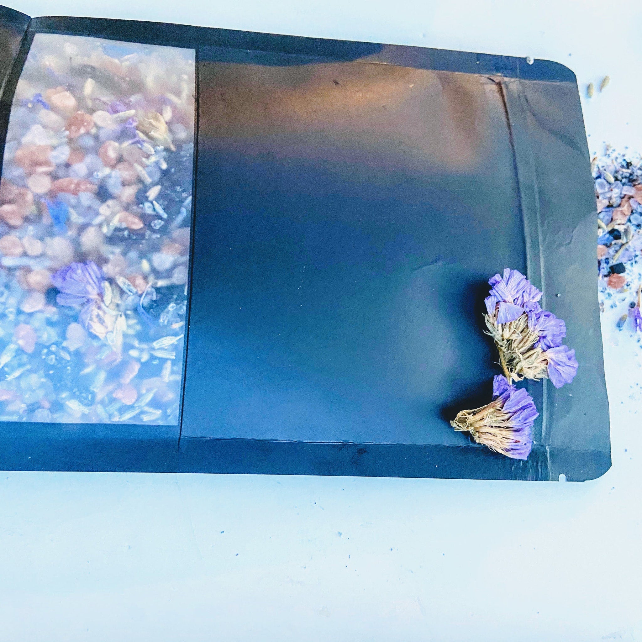 Dried purple flowers with black packaging and clear window, scattered on white surface