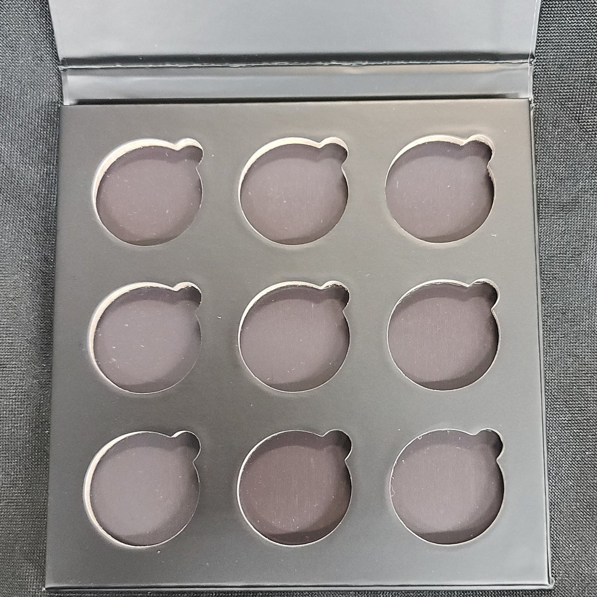 Matte black rectangular eyeshadow palette with nine square pans in neutral shades, magnetic closure