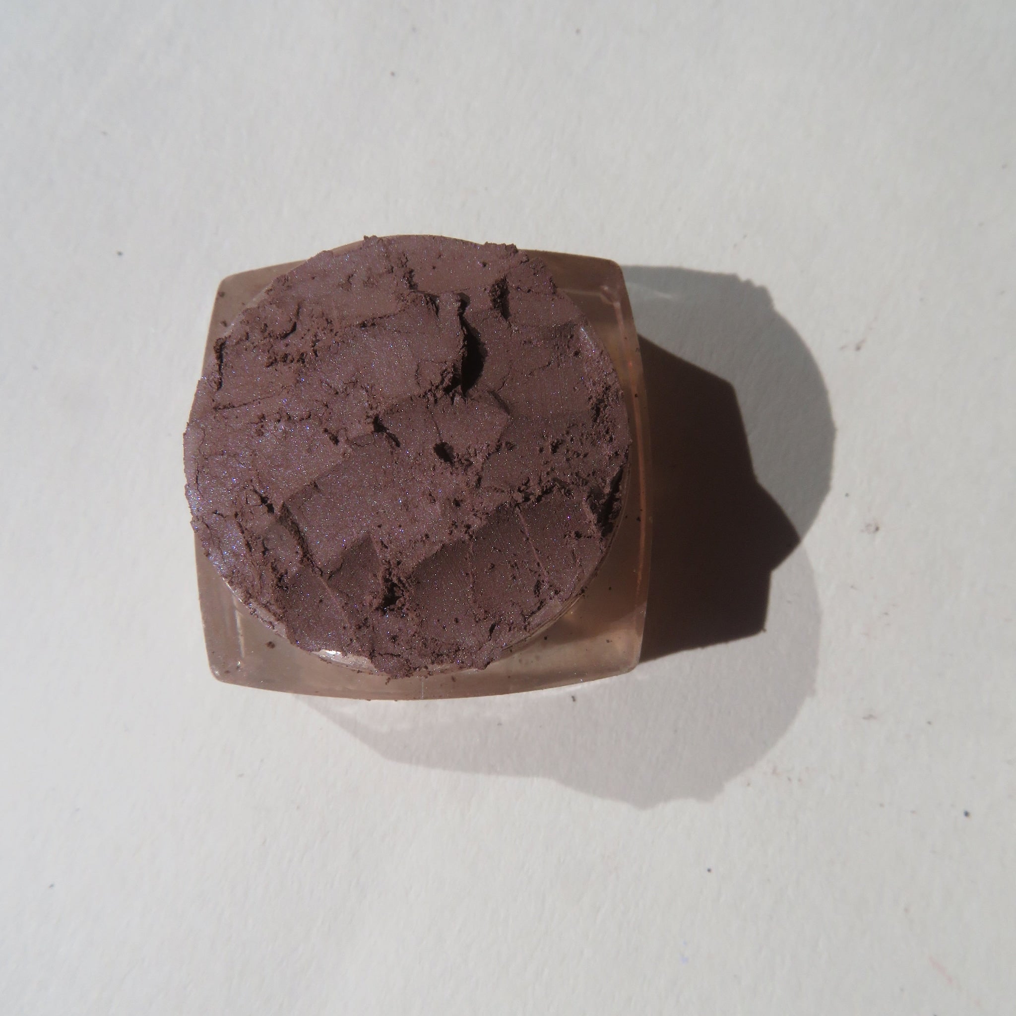 Eyeshadow, dark brown textured powder in clear plastic container, top view