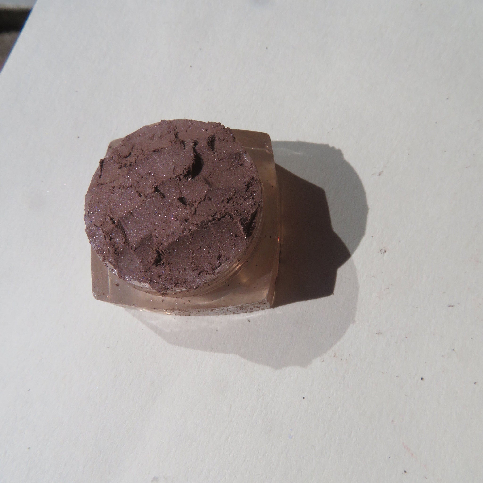 Eyeshadow in brown color with textured surface and clear plastic container