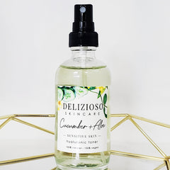 Cucumber toner in clear glass bottle with black spray top, Delizioso Skincare label, and gold geometric stand