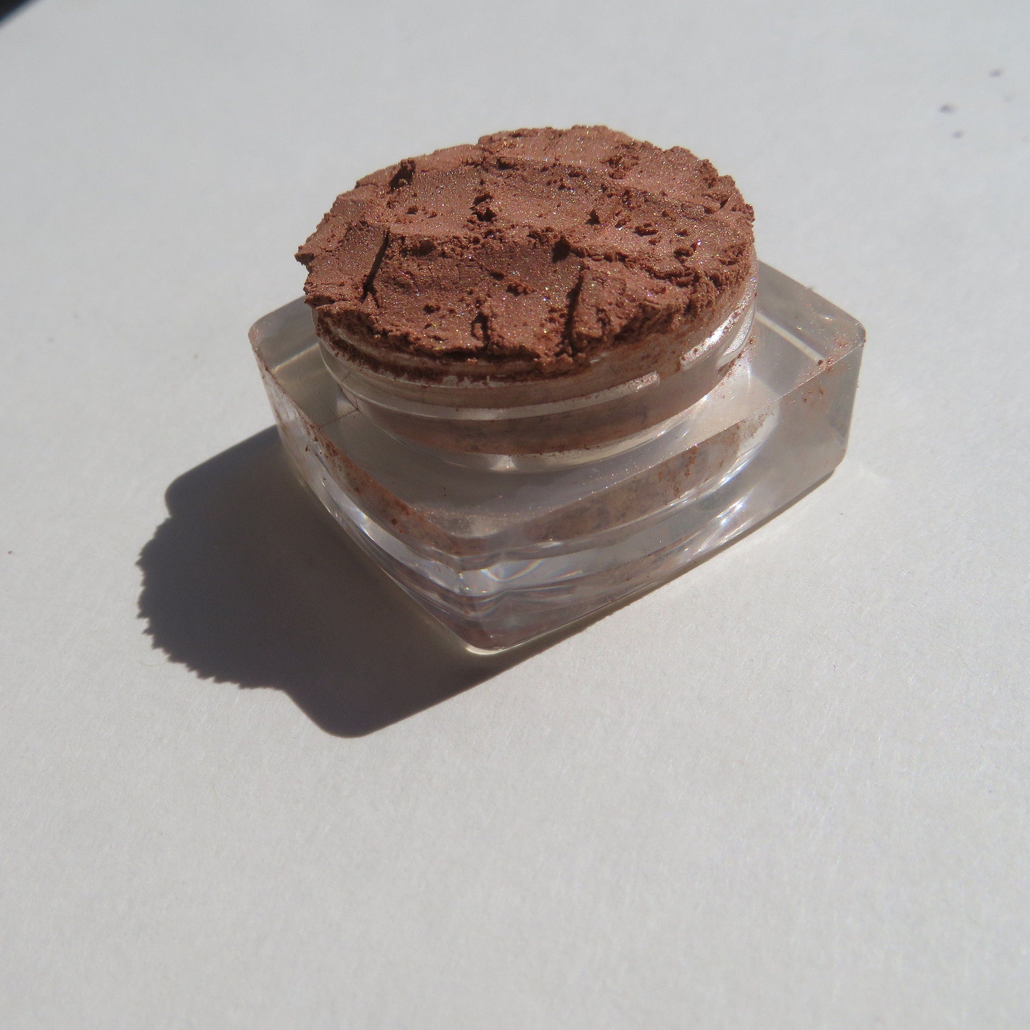 Close-up of loose mineral eyeshadow in bronze copper brown with shimmer particles scattered across surface