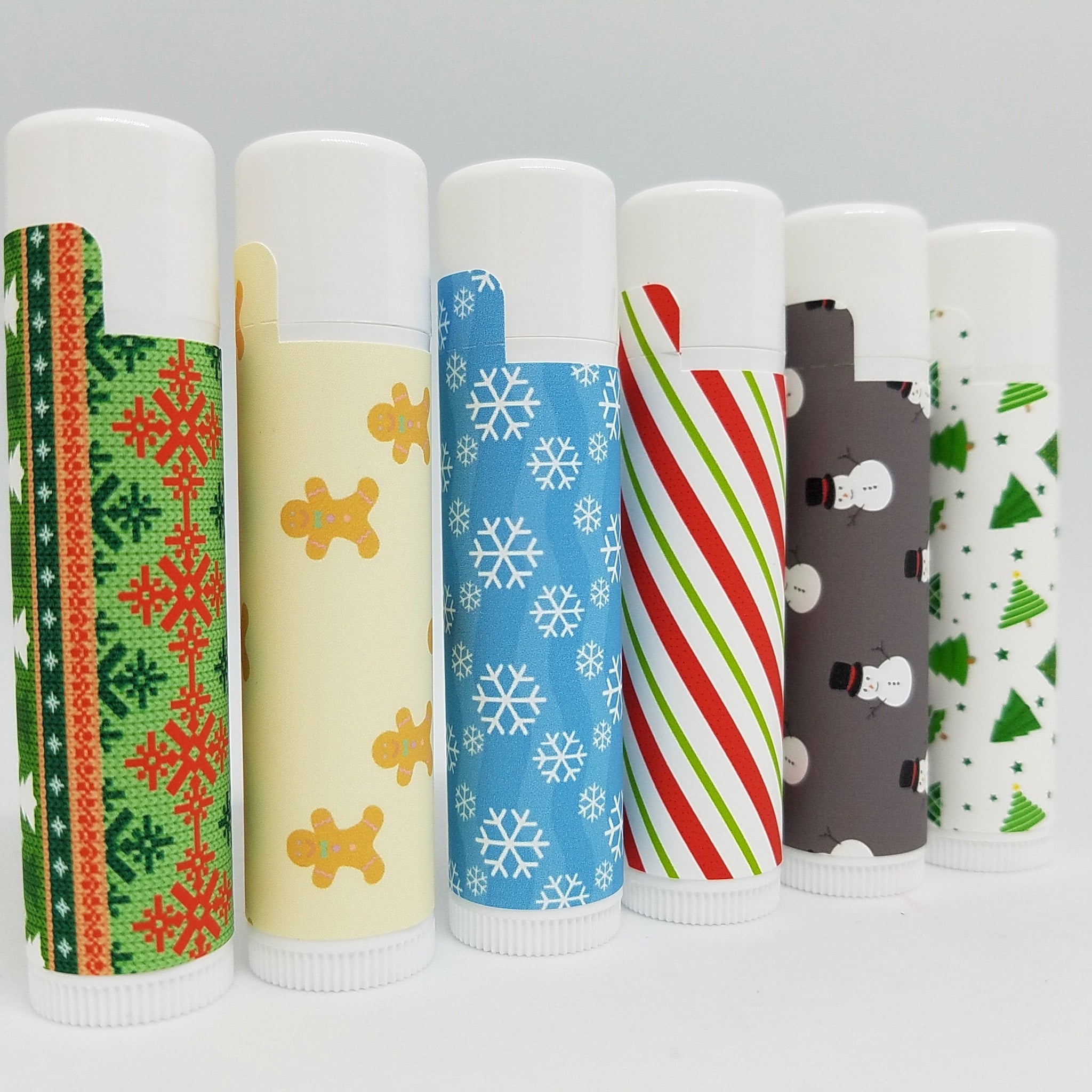 Lip balm tubes with various patterns, including snowflakes, gingerbread men, and stripes, white caps