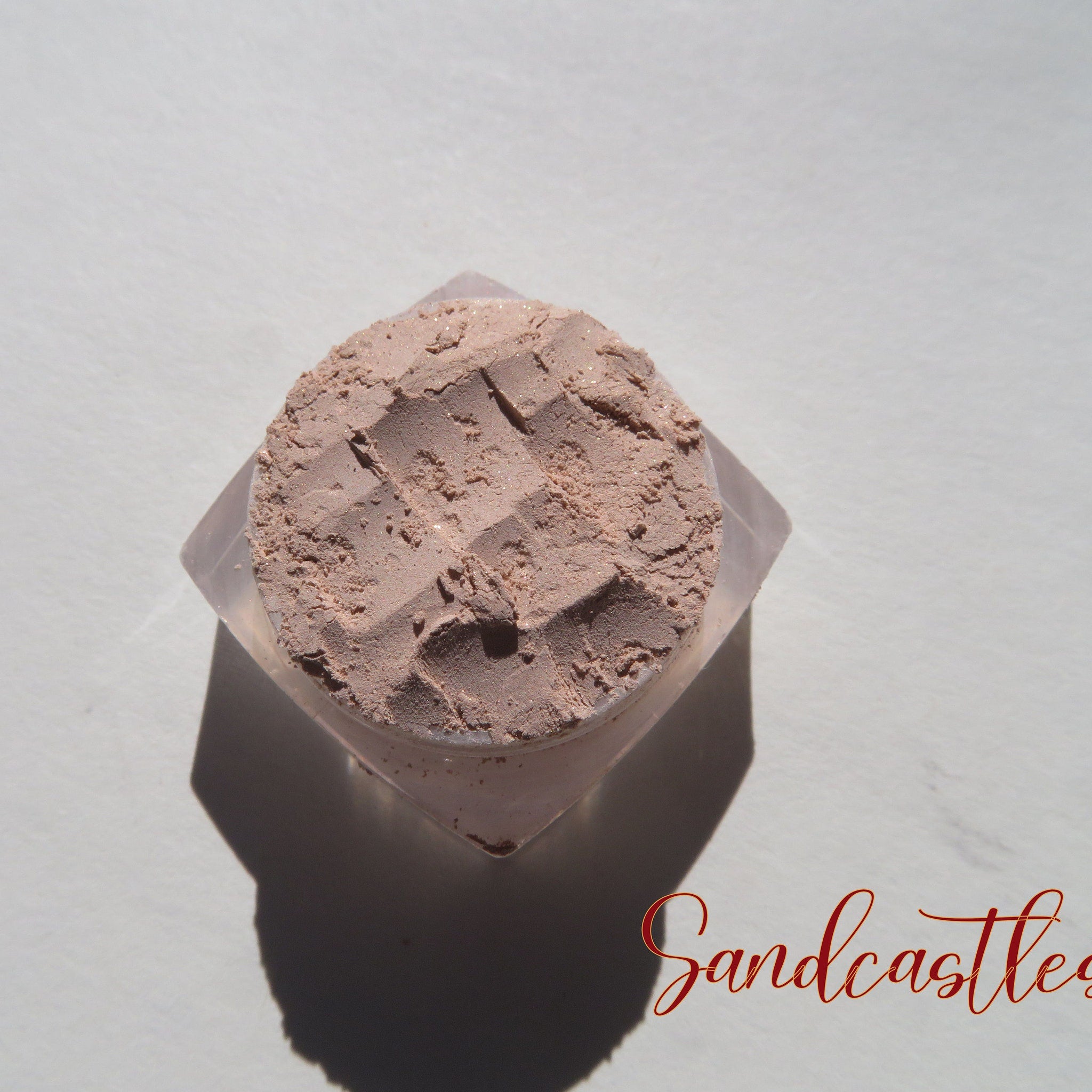 Open jar of SANDCASTLES loose mineral eyeshadow showcasing pale beige shimmer with sandy brown flecks
