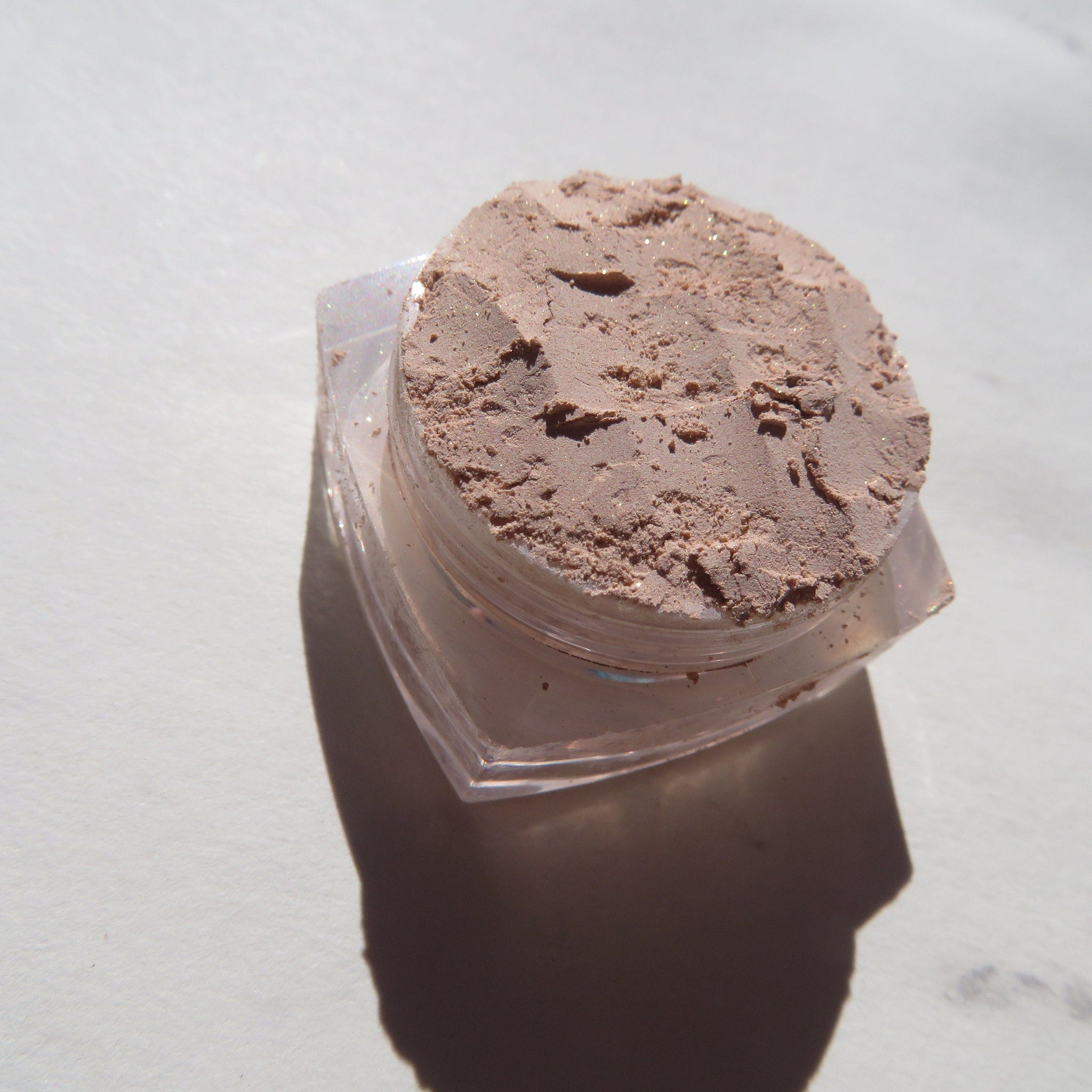 Side view of loose mineral eyeshadow in pale beige with sandy brown shimmer, showcasing eco-friendly vegan pigments