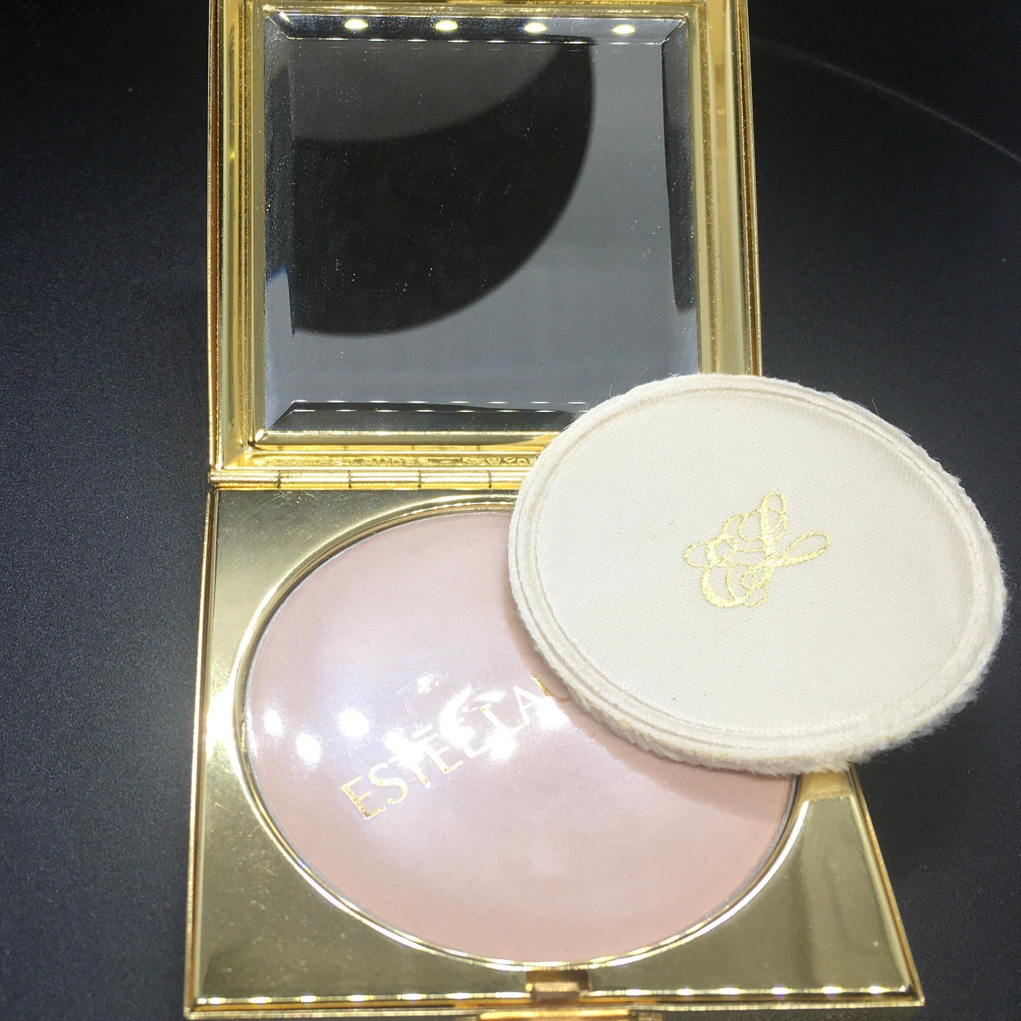 Powder compact with gold frame, pink powder, and white puff with logo detail