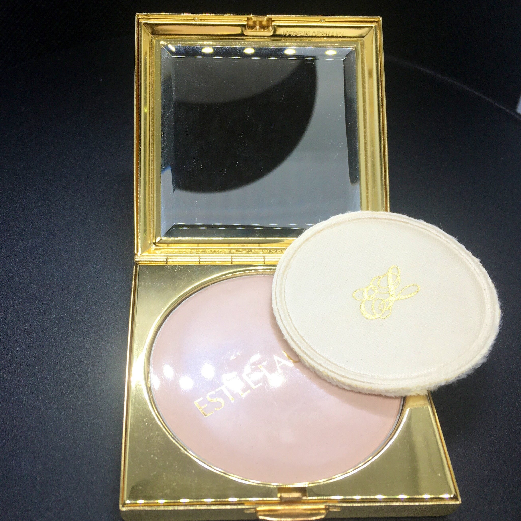 Powder compact with gold frame, pink powder, and Estee Lauder text visible on powder