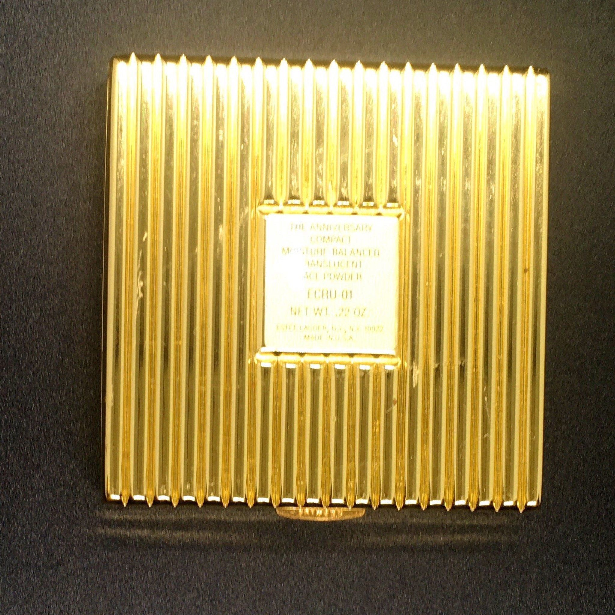 Compact powder case with gold ribbed design and white text label, Estee Lauder brand