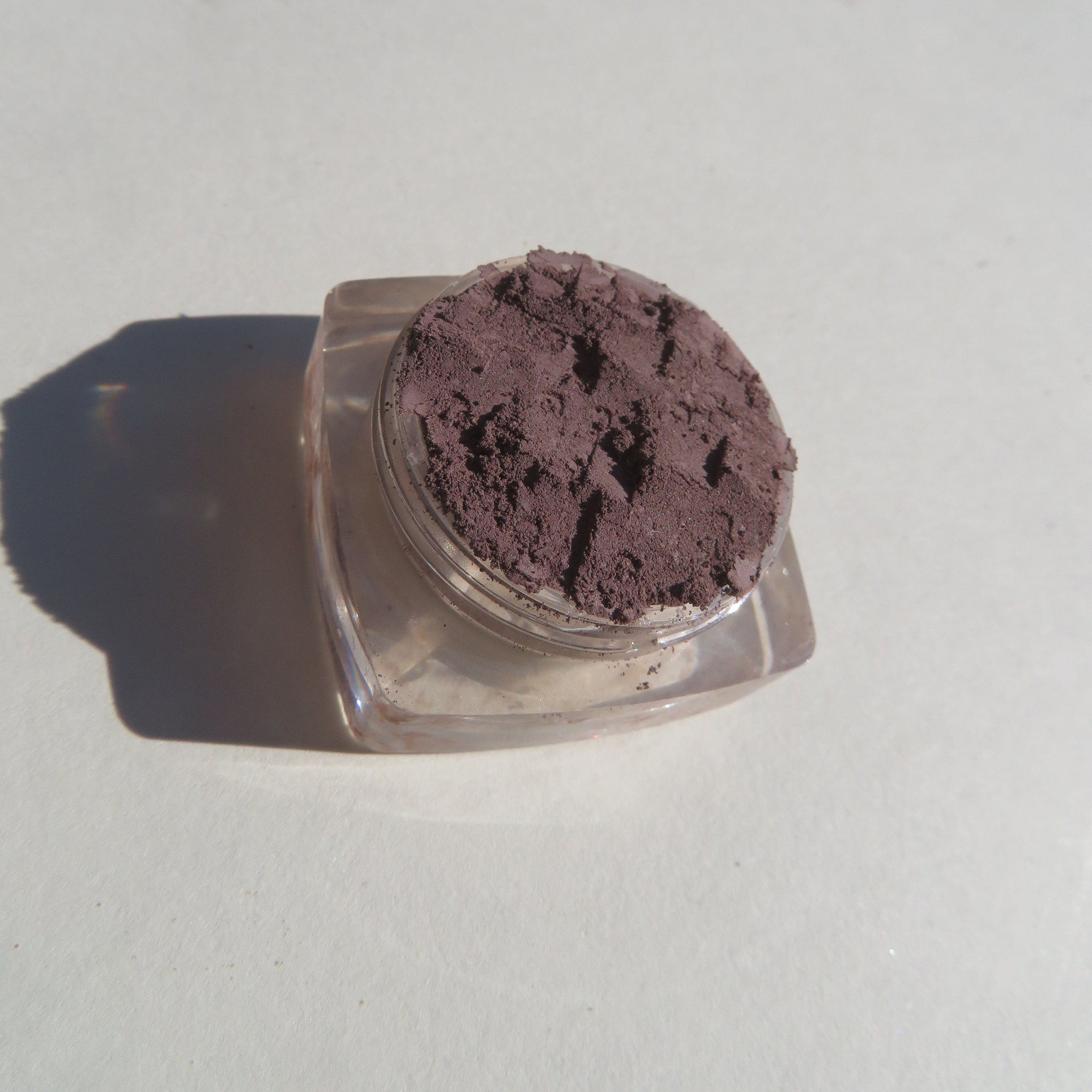 Hand applying matte nutmeg mineral eyeshadow with brush, showing loose pigment texture and warm brown tone.