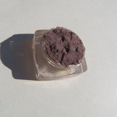 Hand applying matte nutmeg mineral eyeshadow with brush, showing loose pigment texture and warm brown tone.