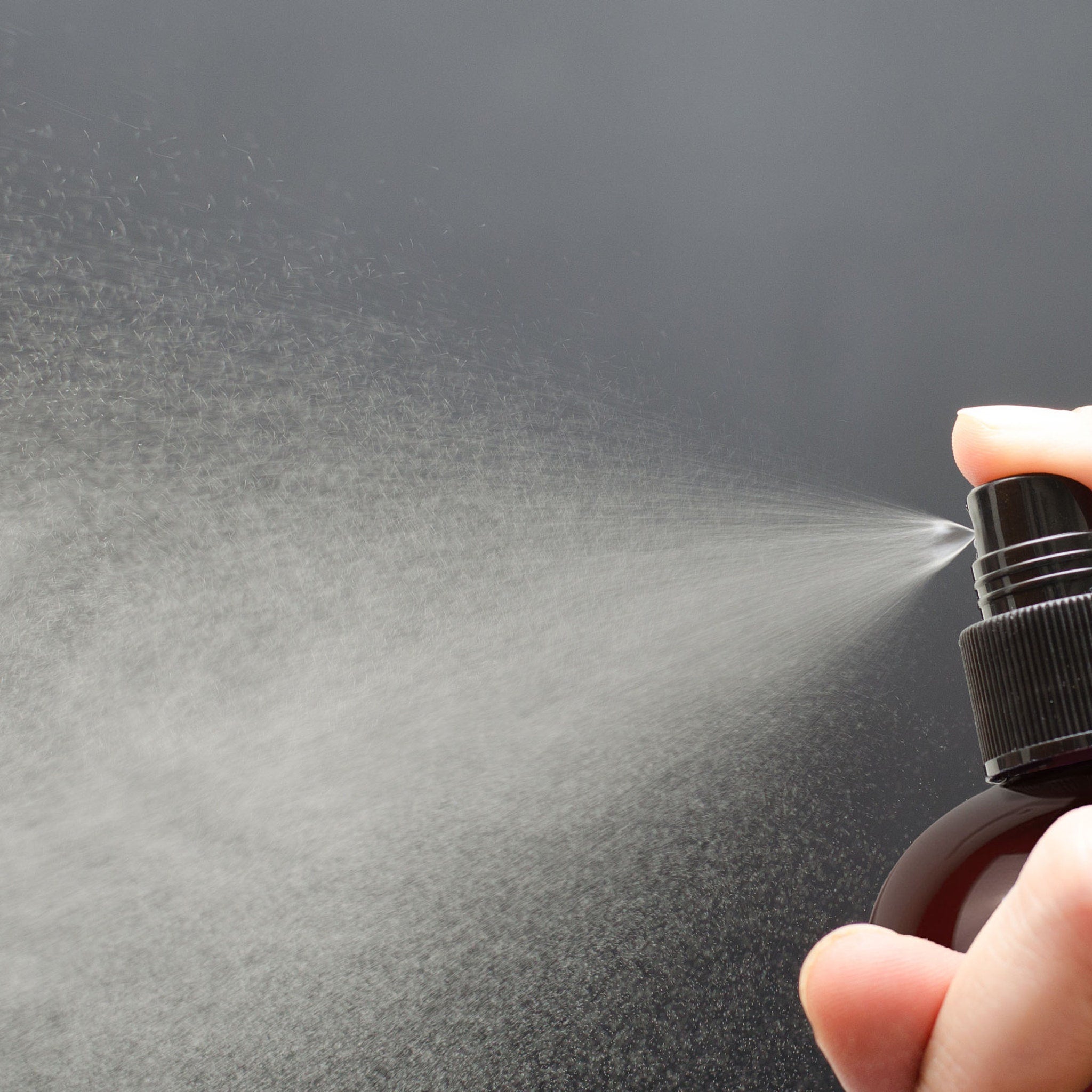 Spray bottle with black cap, brown bottle, and water spray being released