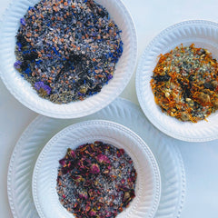 Bath salts with blue, orange, and pink flower petals in white ceramic bowls, top view
