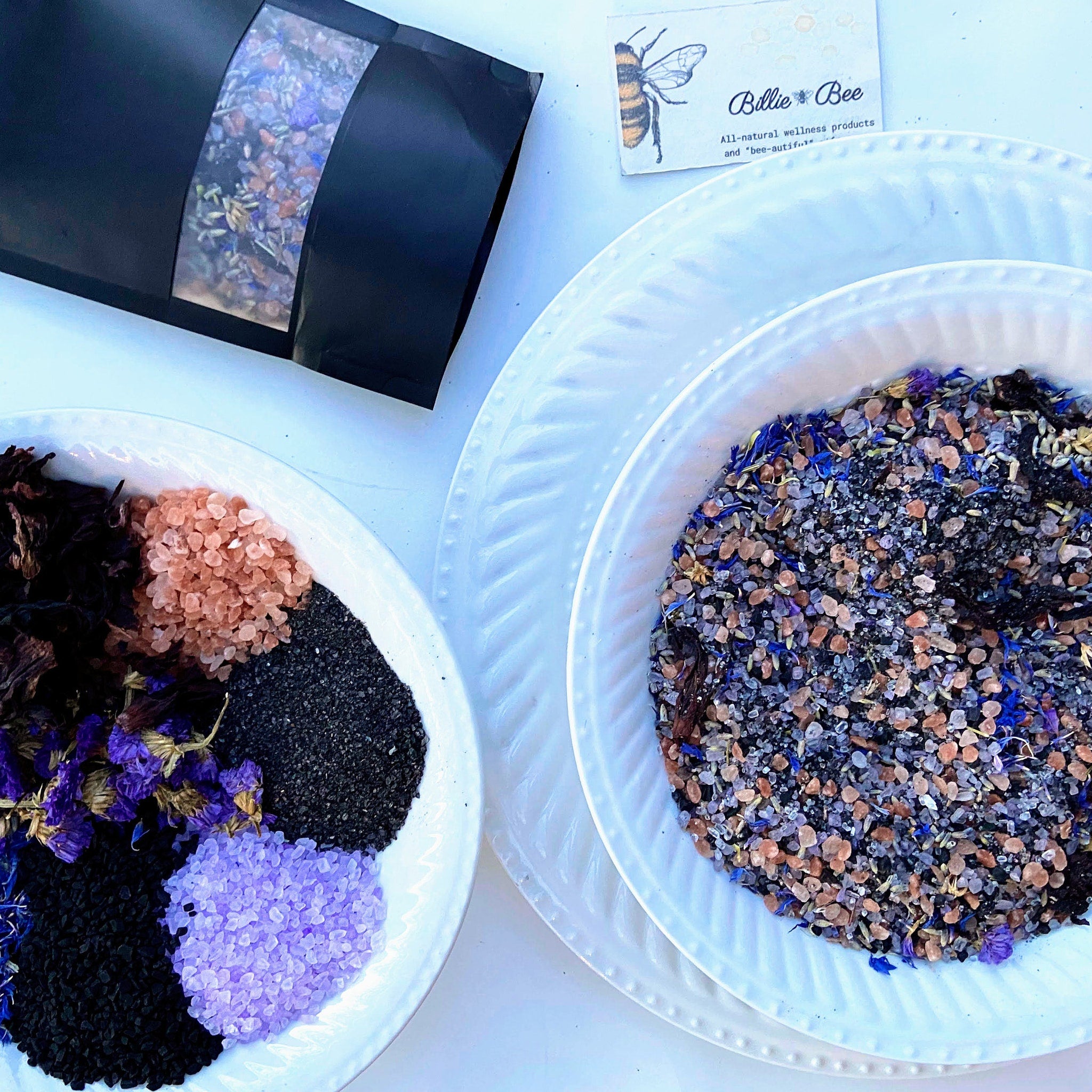 Billie Bee Products logo on a card next to white plates with colorful salts and flowers