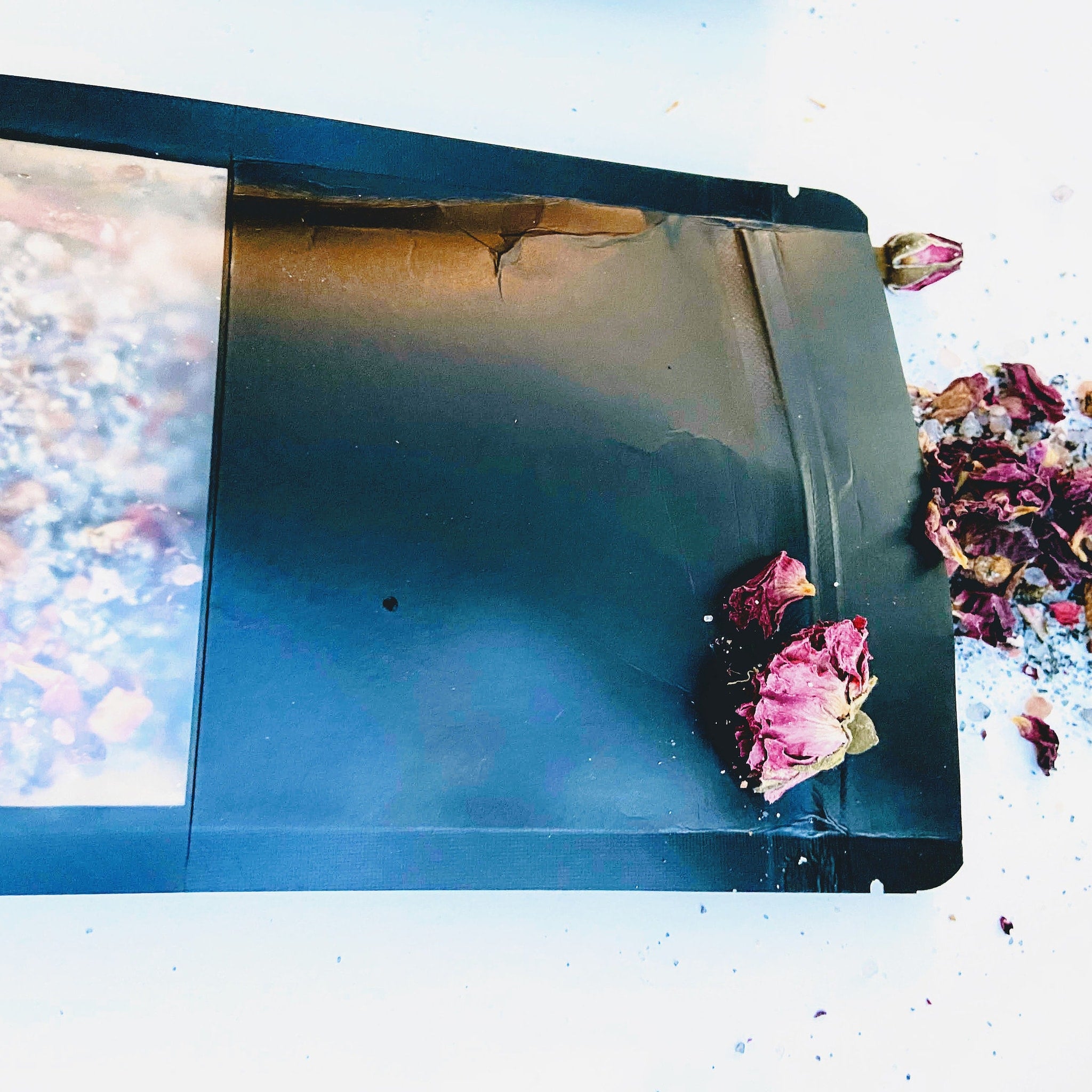 Black paper with clear window, dried rose petals, and white background