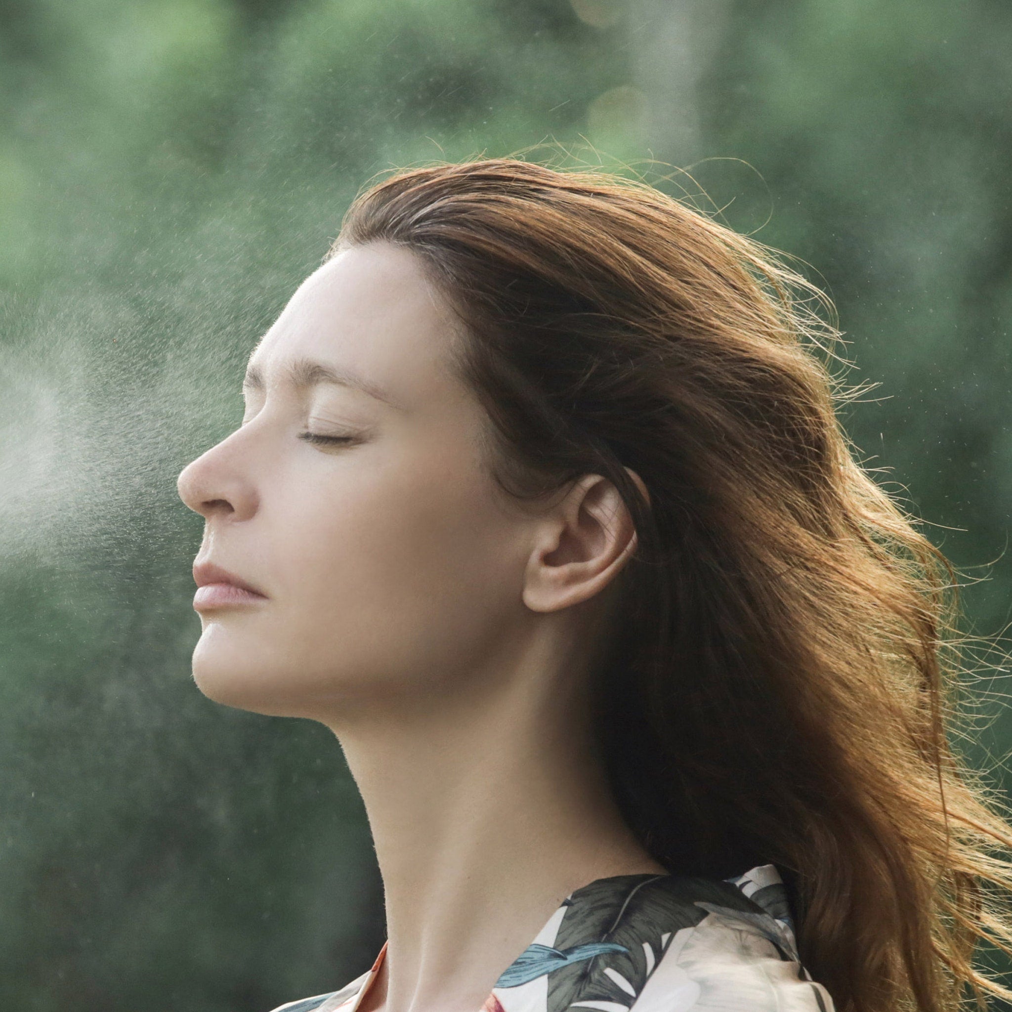 Woman with brown hair and floral patterned top with water mist on face