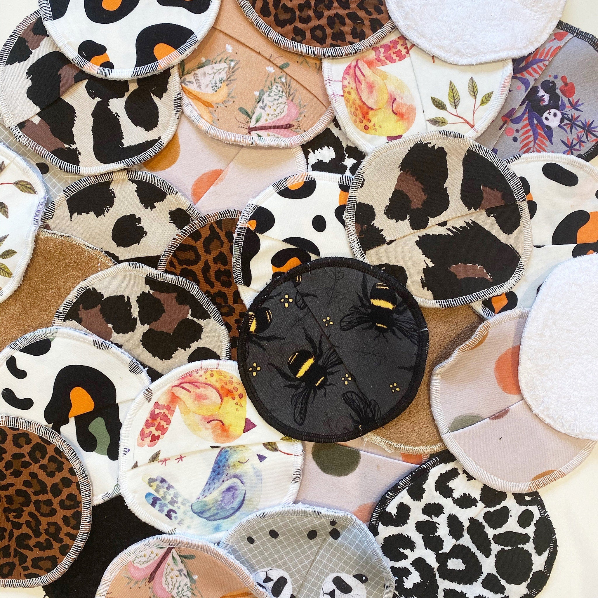 Reusable nursing pads in various patterns, including animal print, floral, and bee designs with white stitching