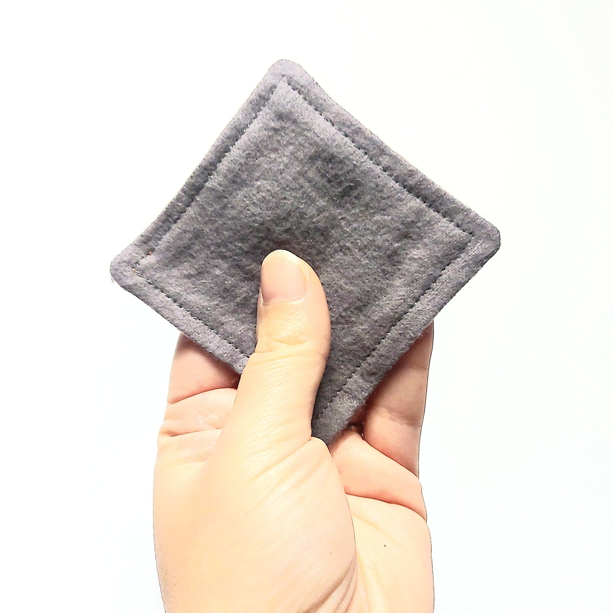 Gray square fabric pad held in hand, with stitched edges and soft material