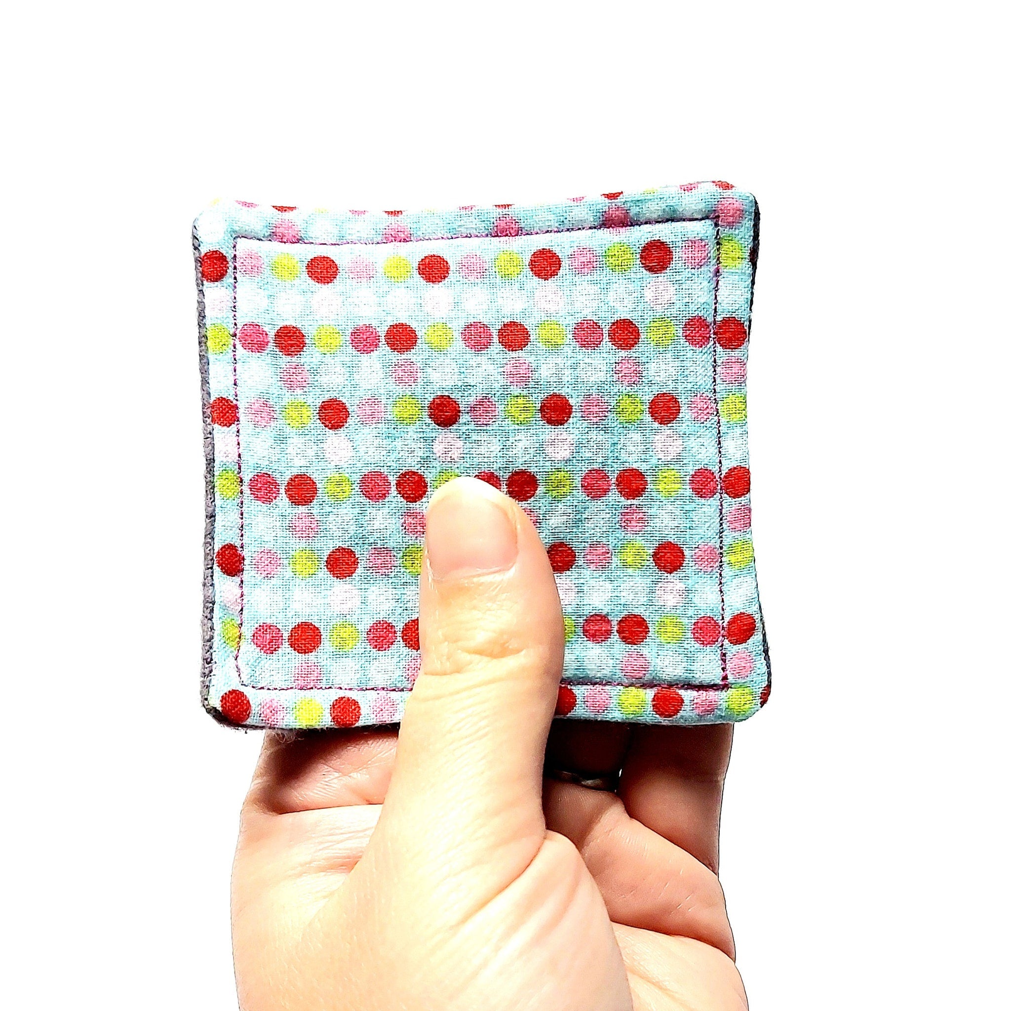 Polka dot fabric square with blue, red, pink, and yellow dots, held by a hand, showing the fabric texture and pattern