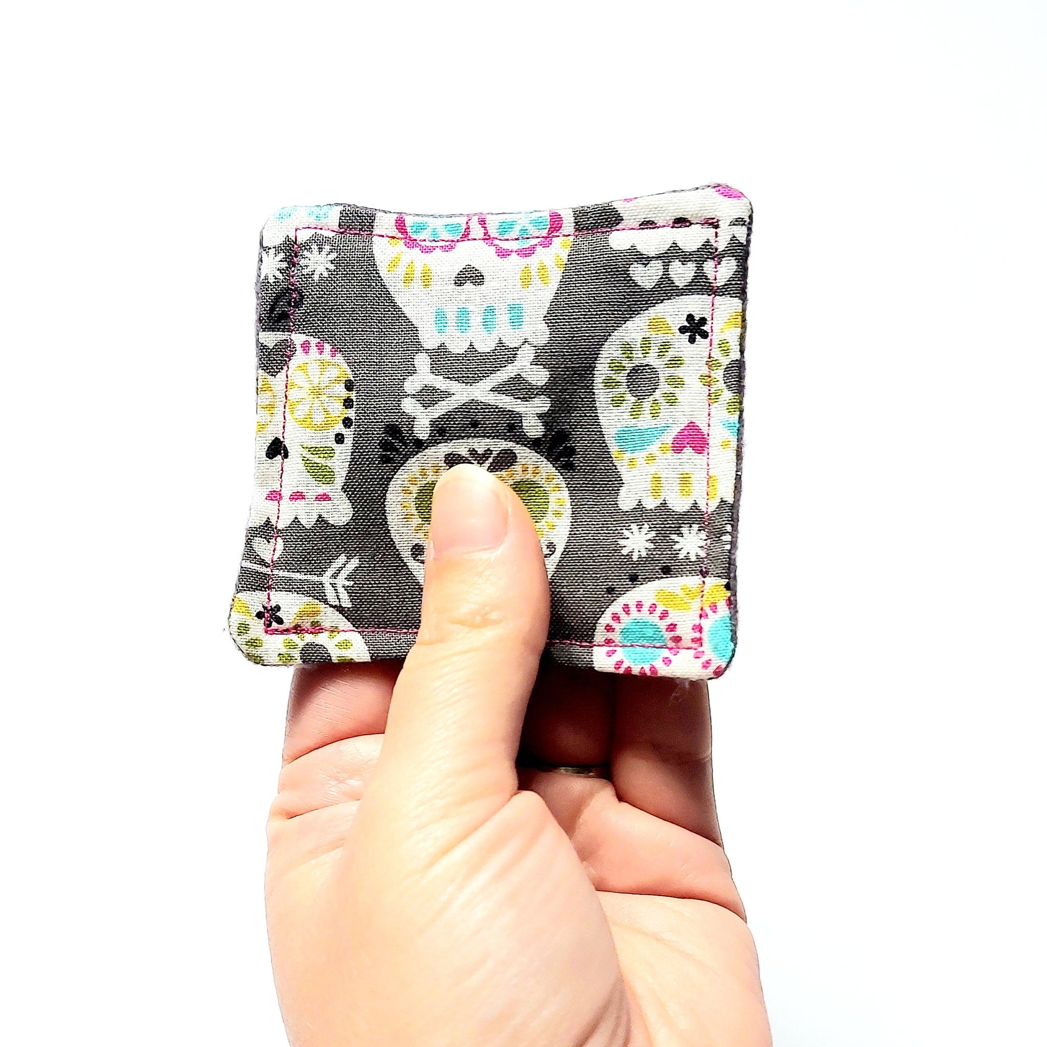 Square fabric item with skull pattern, gray background, and pink stitching held by hand